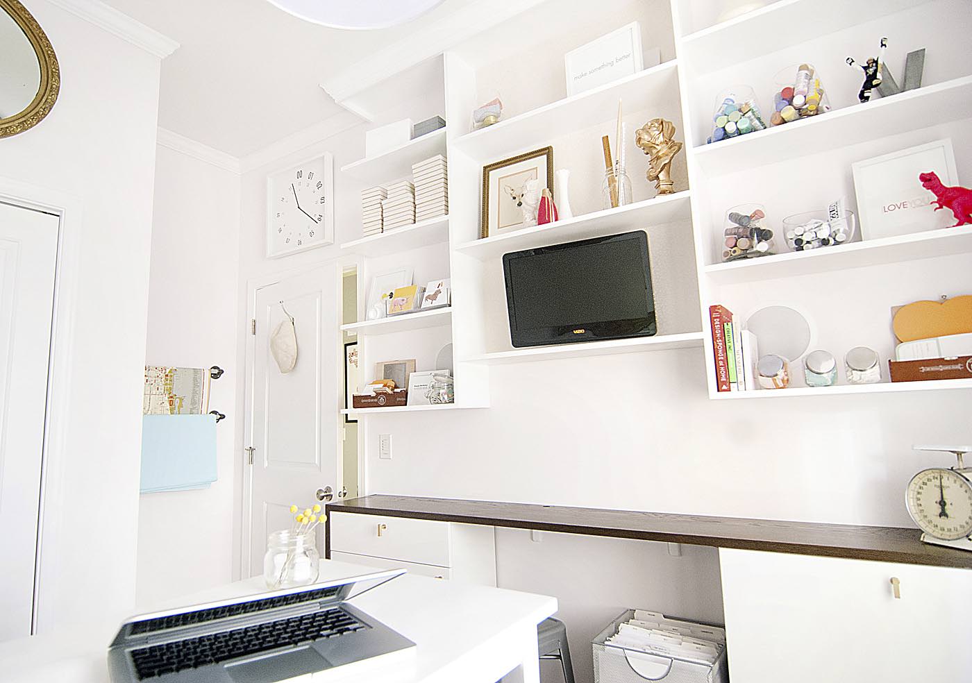A light colored studio office space with custom built-in shelves and a high work table. 