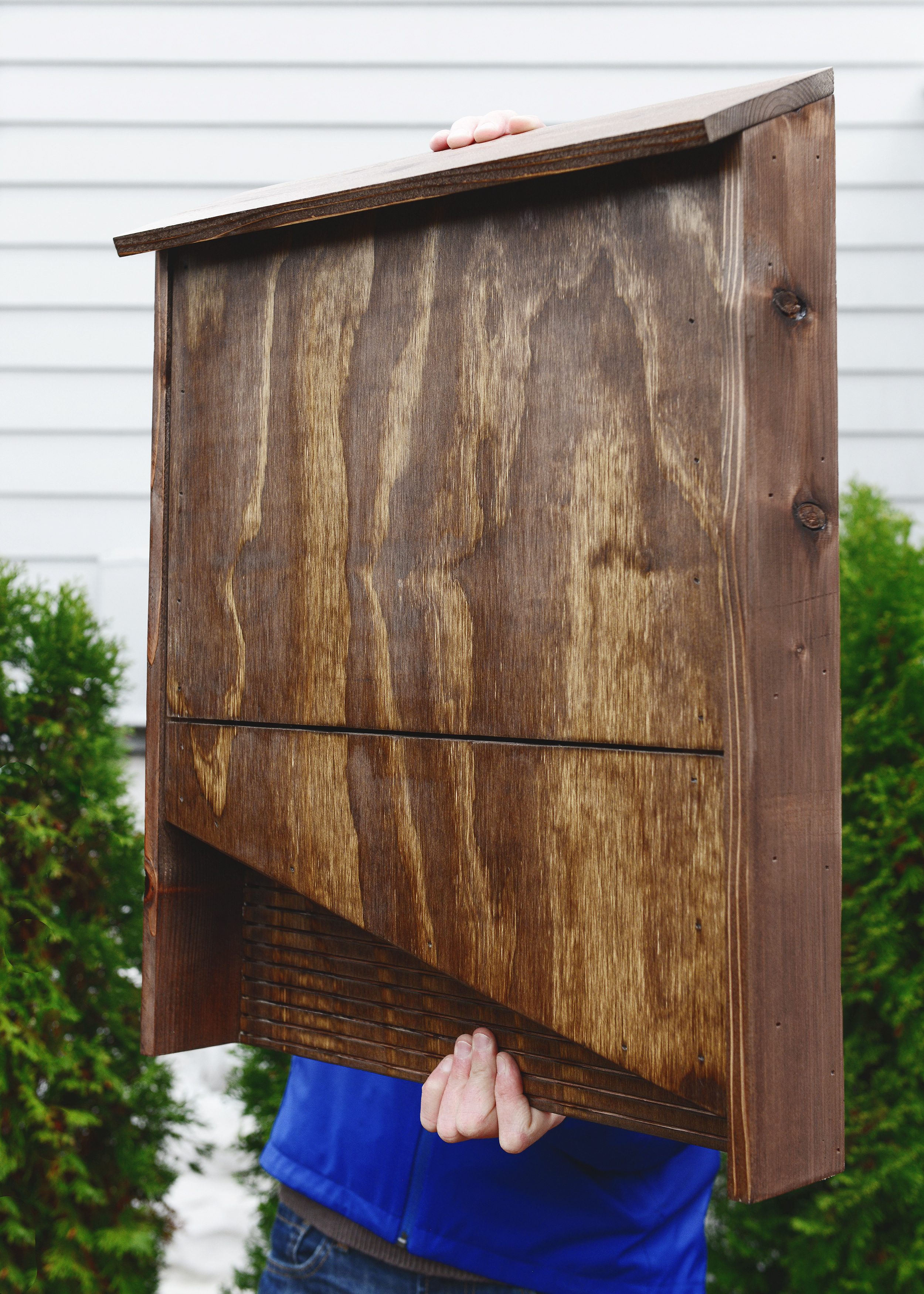 A completed DIY bat box is held up in an urban backyard // How-to build a bat box, DIY bat box via Yellow Brick Home