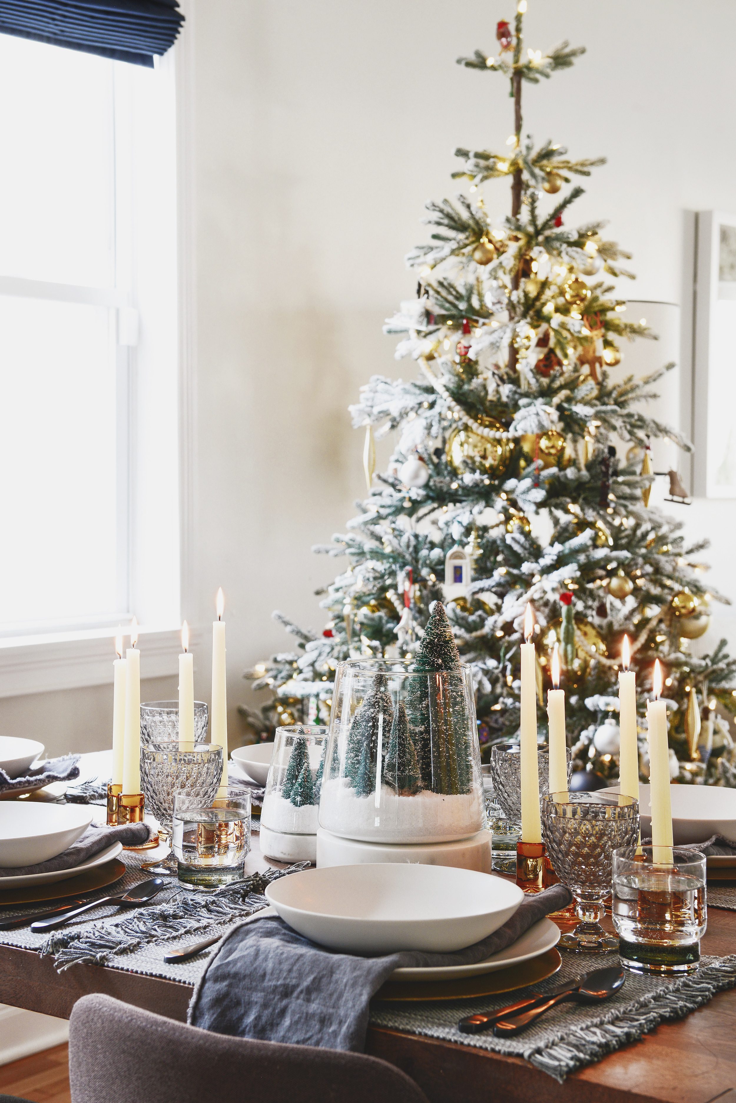 A holiday table setting in shades of grey, amber and white and a Christmas tree in the background | This holiday season, consider simplifying your table setting with these 5 fresh styling tips! | via Yellow Brick Home