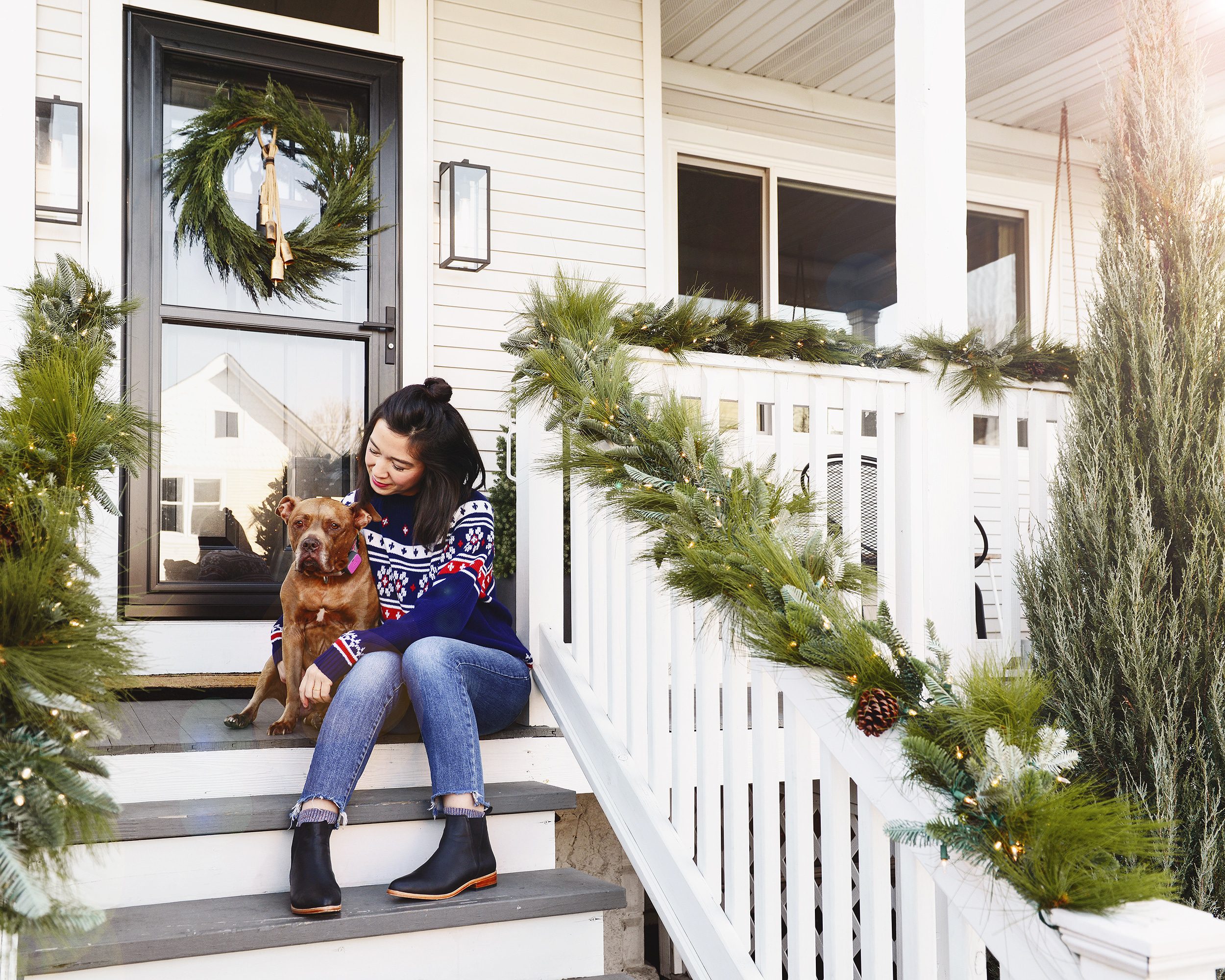 Kim and CC sitting on our front porch, with garland on the railings and a wreath on the door | Yellow Brick Home holiday home