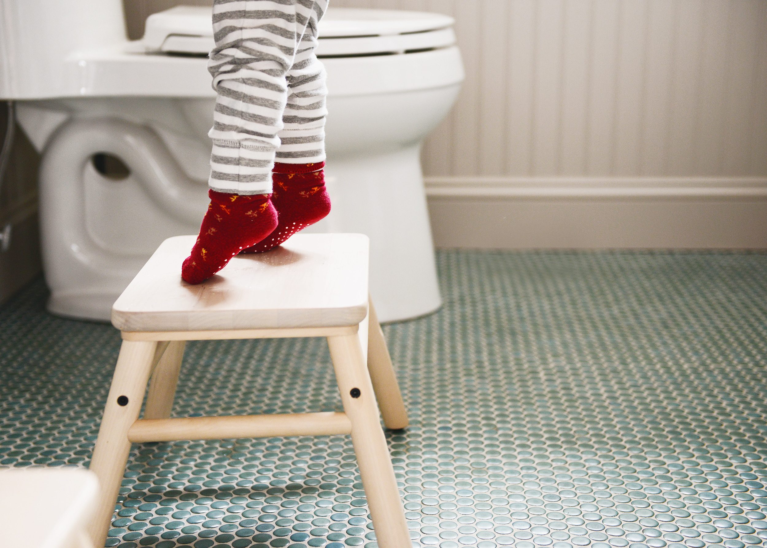 A toddler stands on tip toes on a step stool in a green and tan bathroom // via Yellow Brick Home