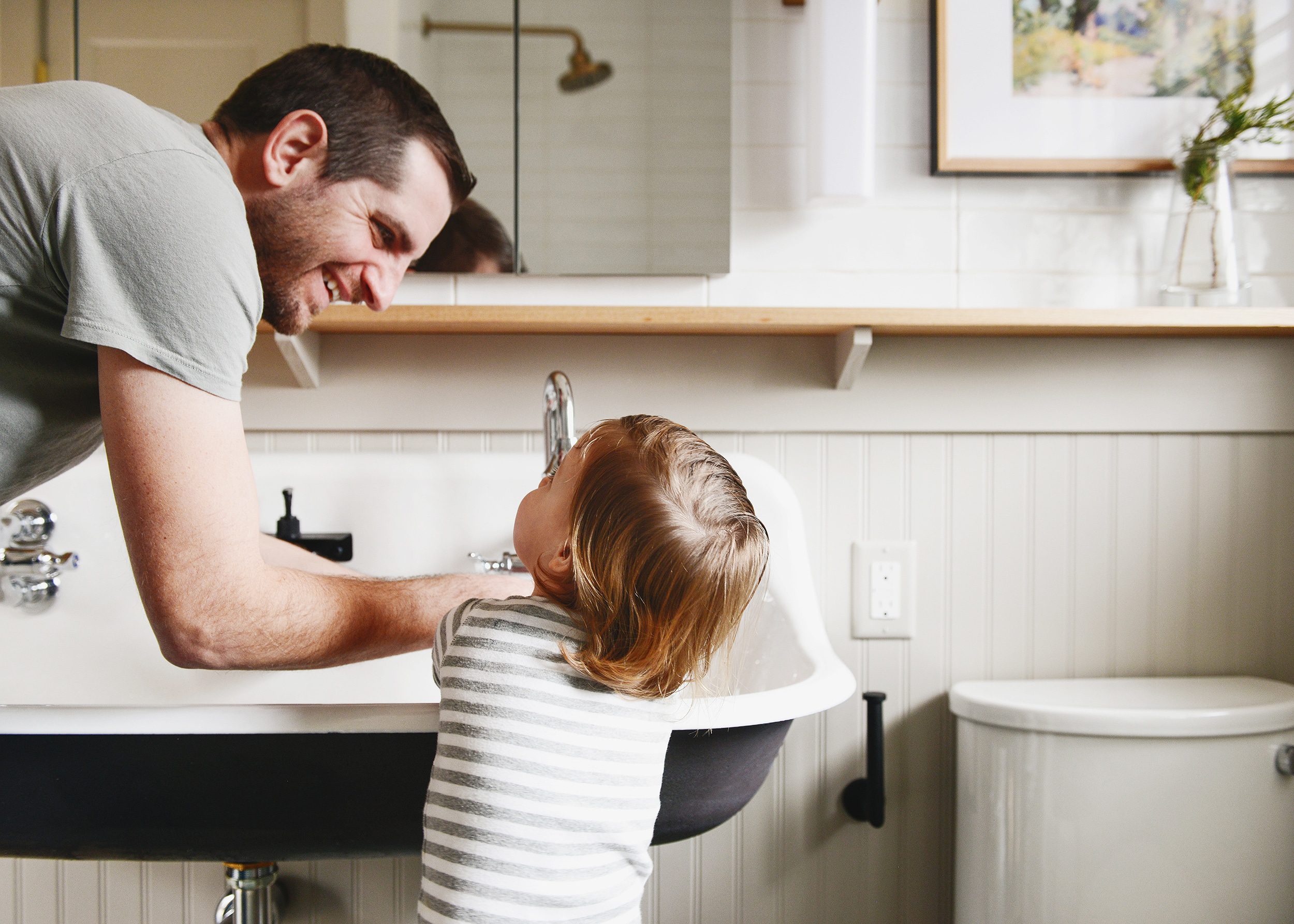 A father and toddler wash their hands together in a large basin sink in a tan and green bathroom // via Yellow Brick Home
