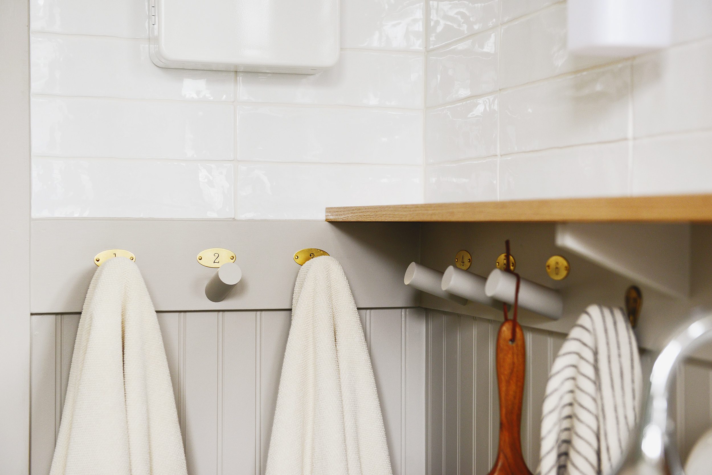 Beige towels hang on six wooden towel hooks integrated into a beadboard wall // via Yellow Brick Home