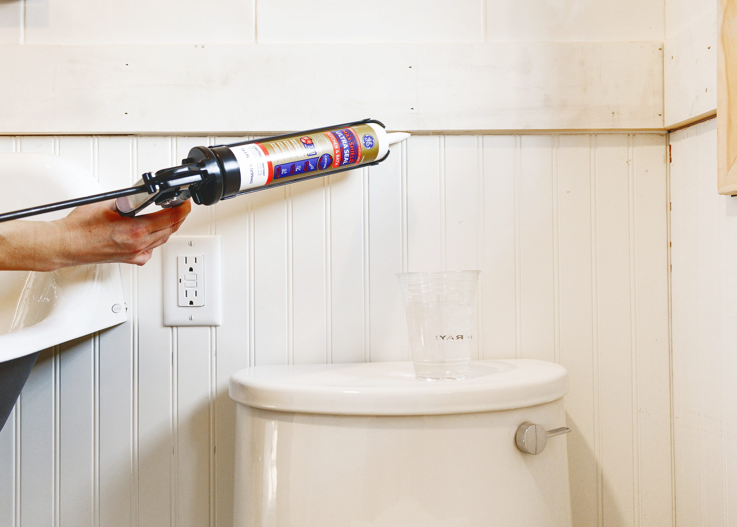 A caulk gun is used to fill the seam between a beadboard panel and a top cap. 