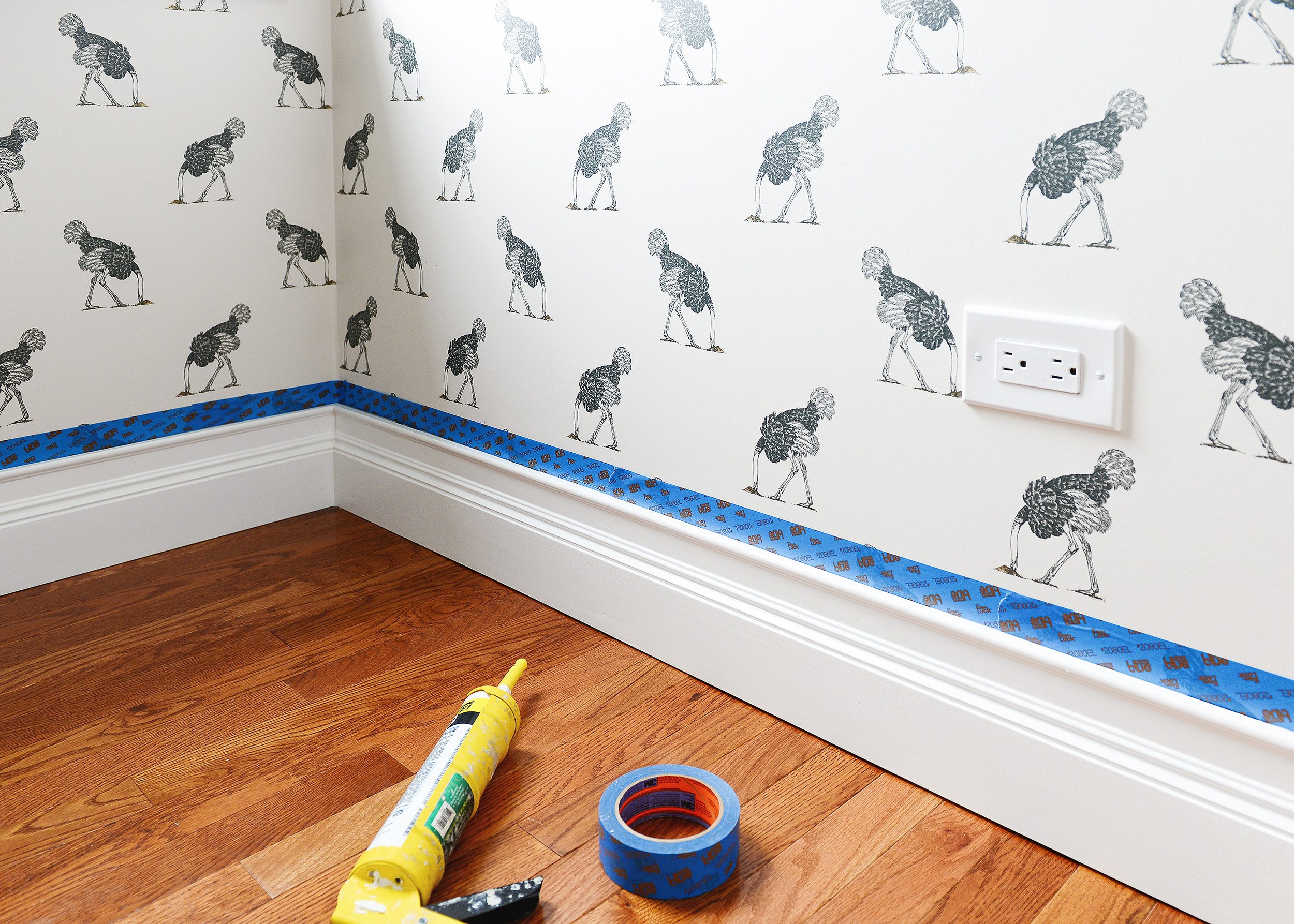 Taping off a caulk line where the baseboard meets the wallpaper | via Yellow Brick Home