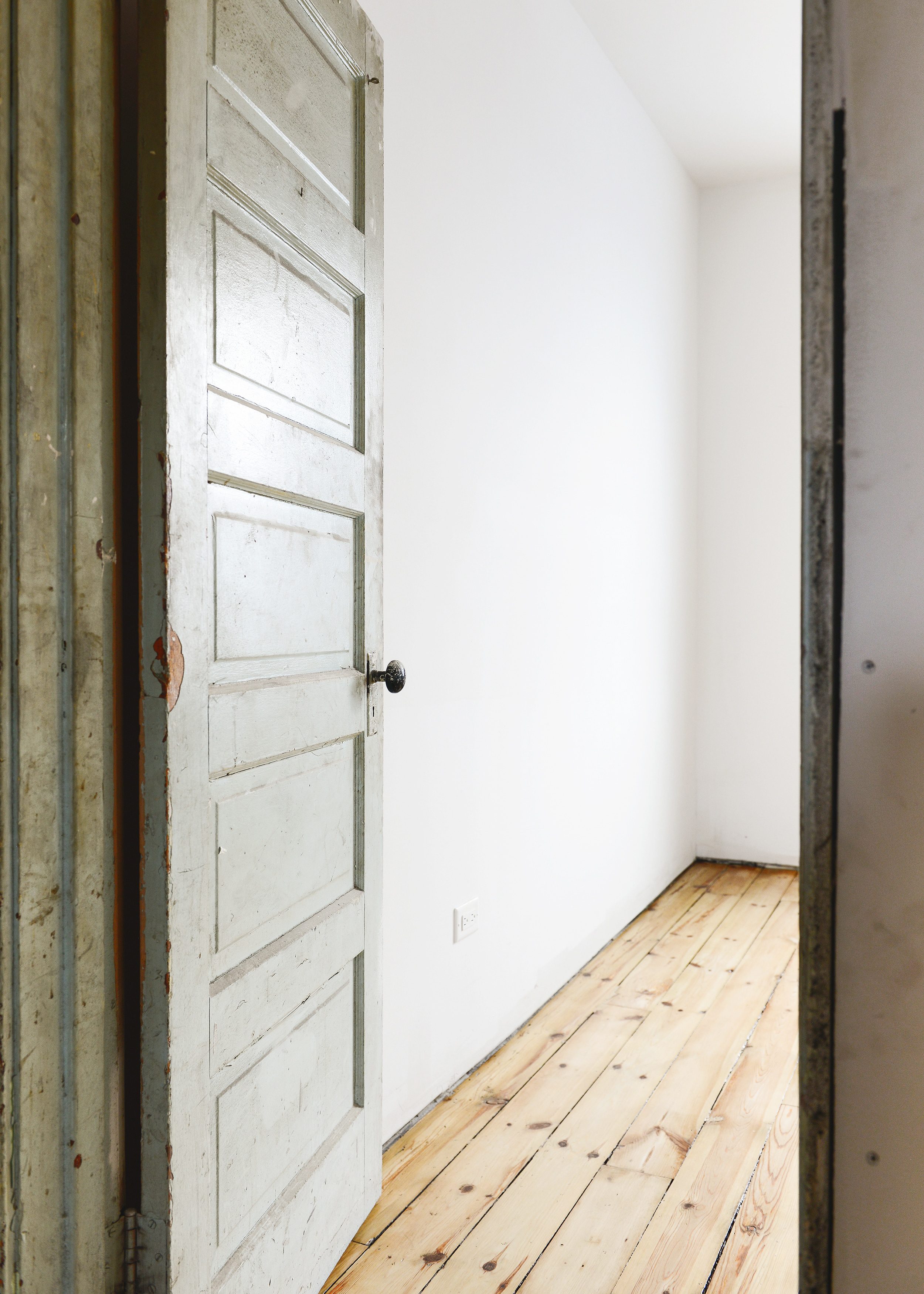 A vintage door opens into a white bedroom with refinished wide plank pine flooring // via Yellow Brick Home