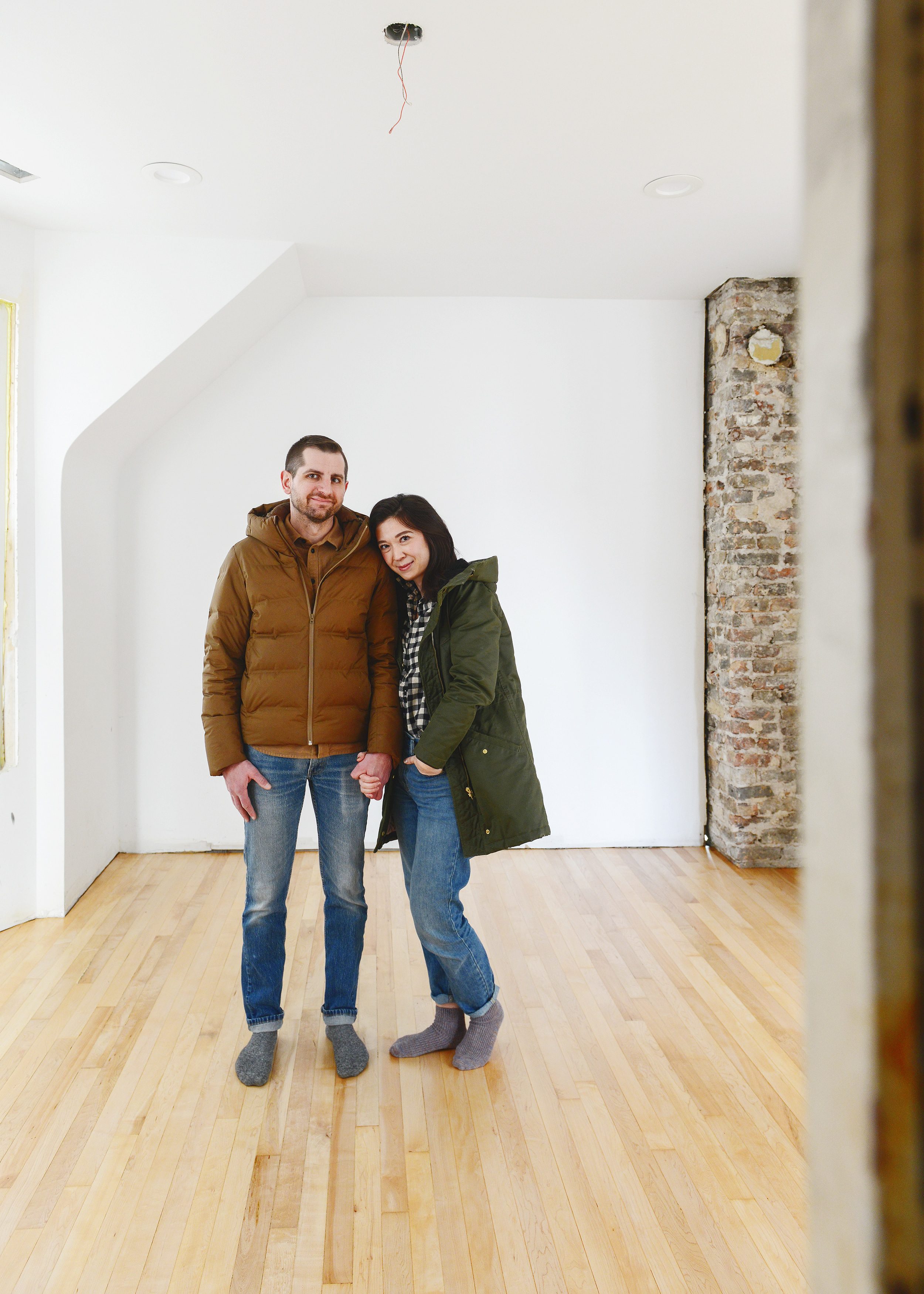 A couple holding hands in winter coats, wearing no shoes atop newly refinished hardwood flooring in a vintage Chicago home // via Yellow Brick Home