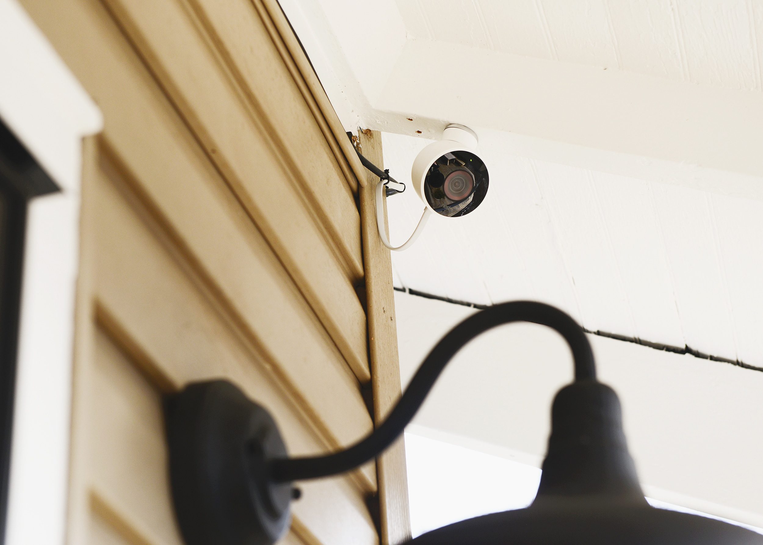 An outdoor security camera blends seamlessly with the white ceiling truss it is connected to // via yellow brick home