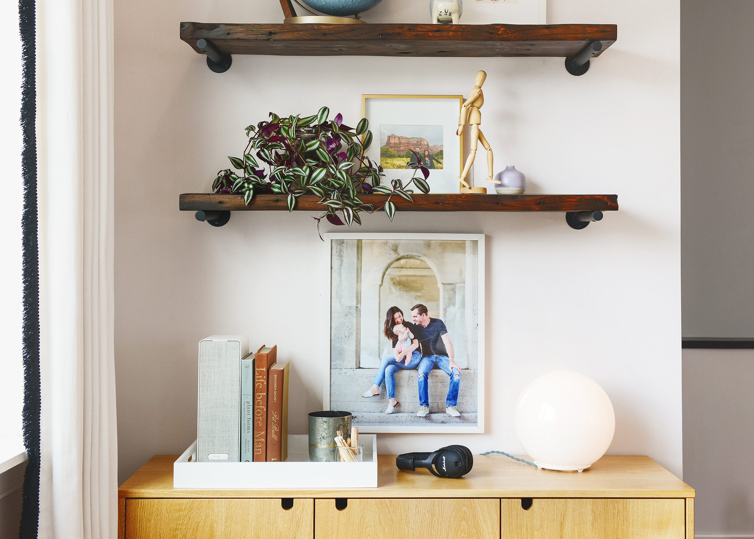 The top of an oak credenza holds a tray full of books, candles, headphones. Above it, vintage shelves hold plants and decor items // via Yellow Brick Home