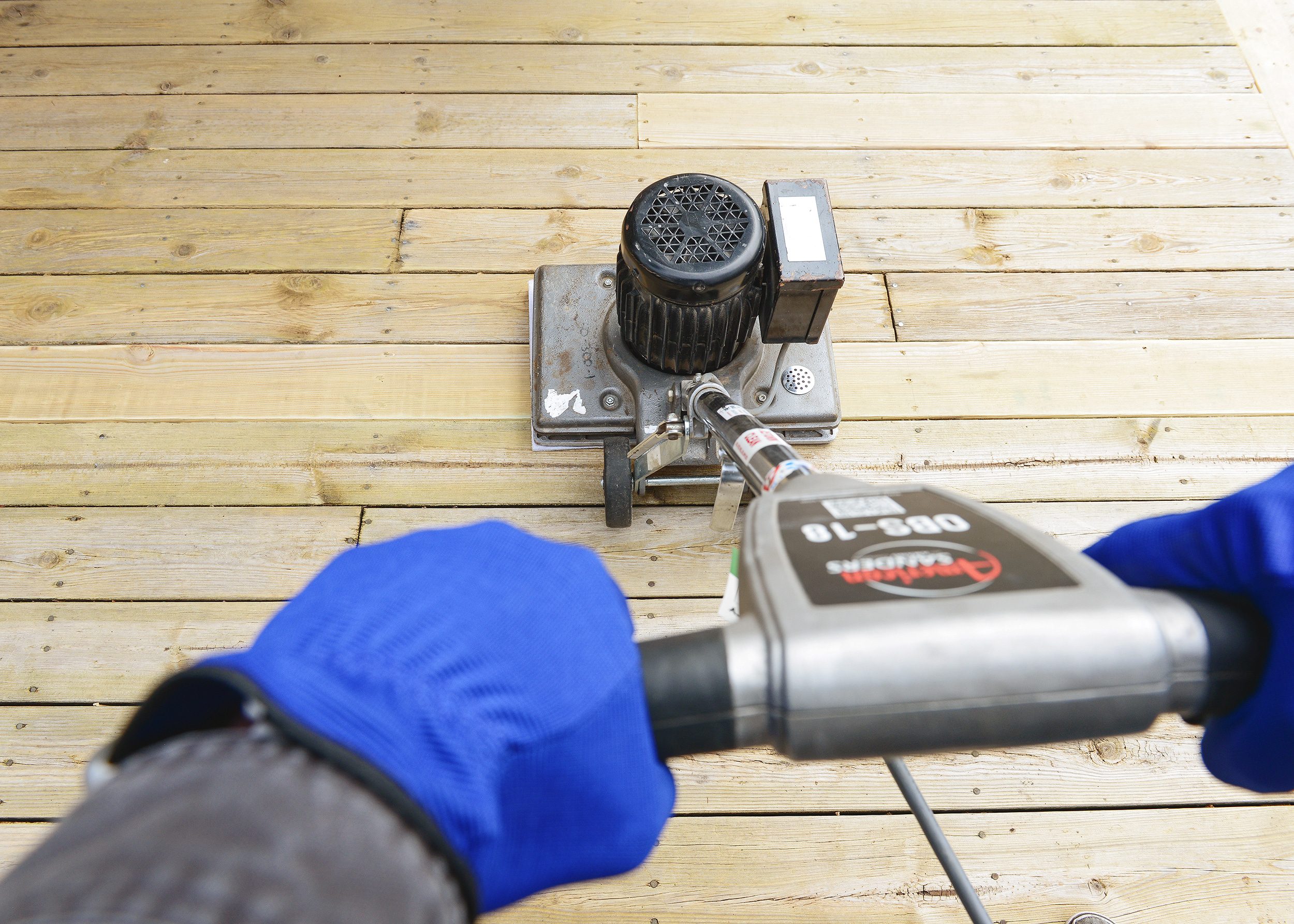 Hands adorned in blue work gloves control an industrial floor sander being used on a deck surface // via Yellow Brick Home