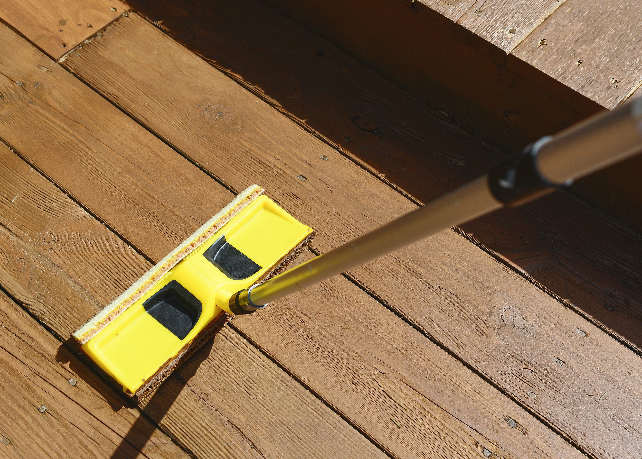 A staining pad is used to apply warm brown stain to a deck // via Yellow Brick Home