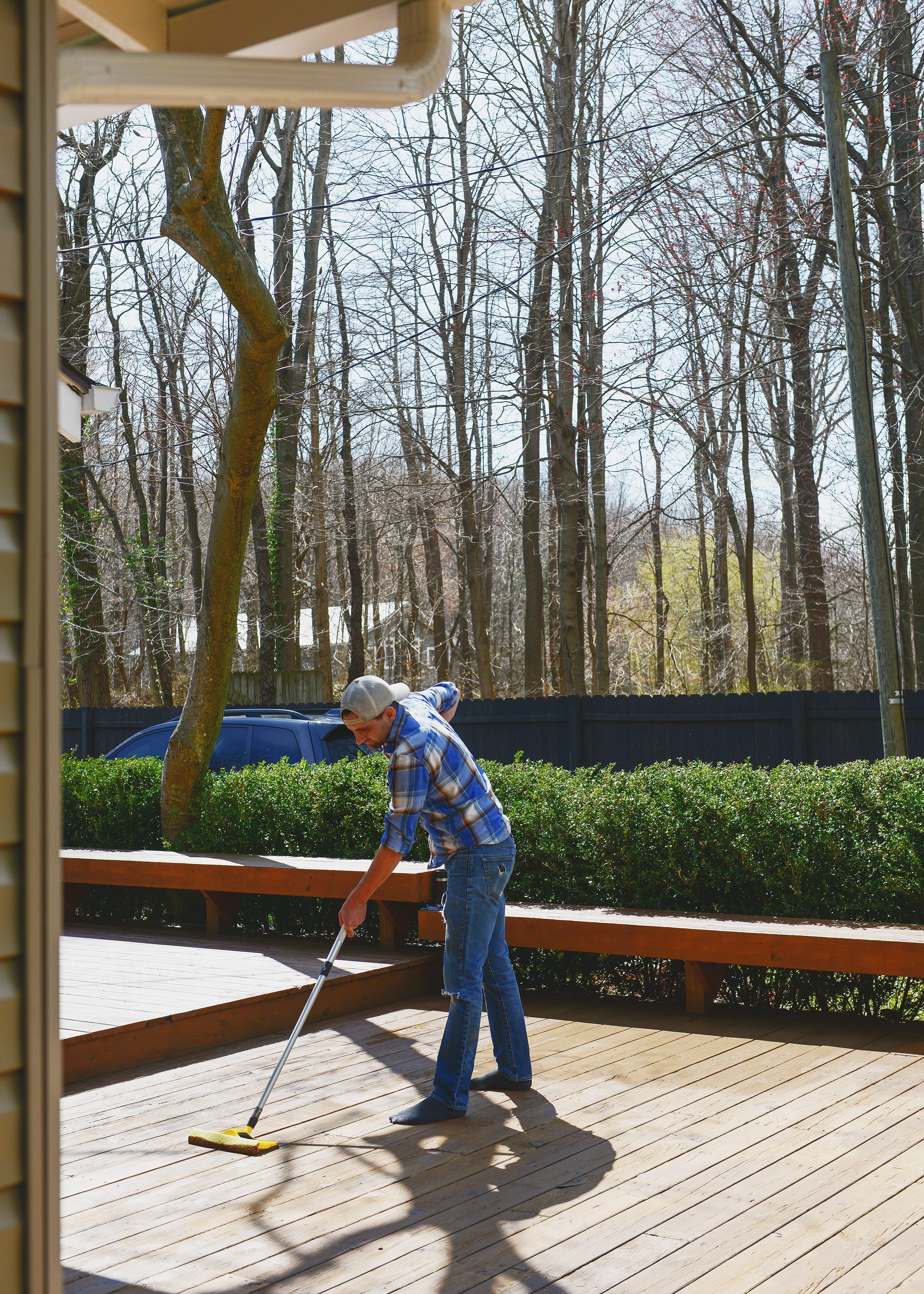 A man in an ugly plaid work shirt applies stain to a deck in springtime // via Yellow Brick Home