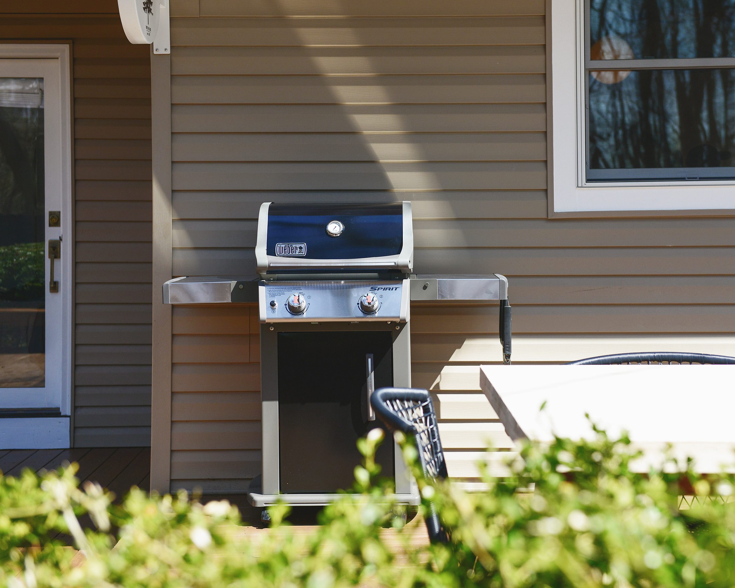 A new weber gas grill sits on a freshly stained deck at the front of a tan house // via Yellow Brick Home