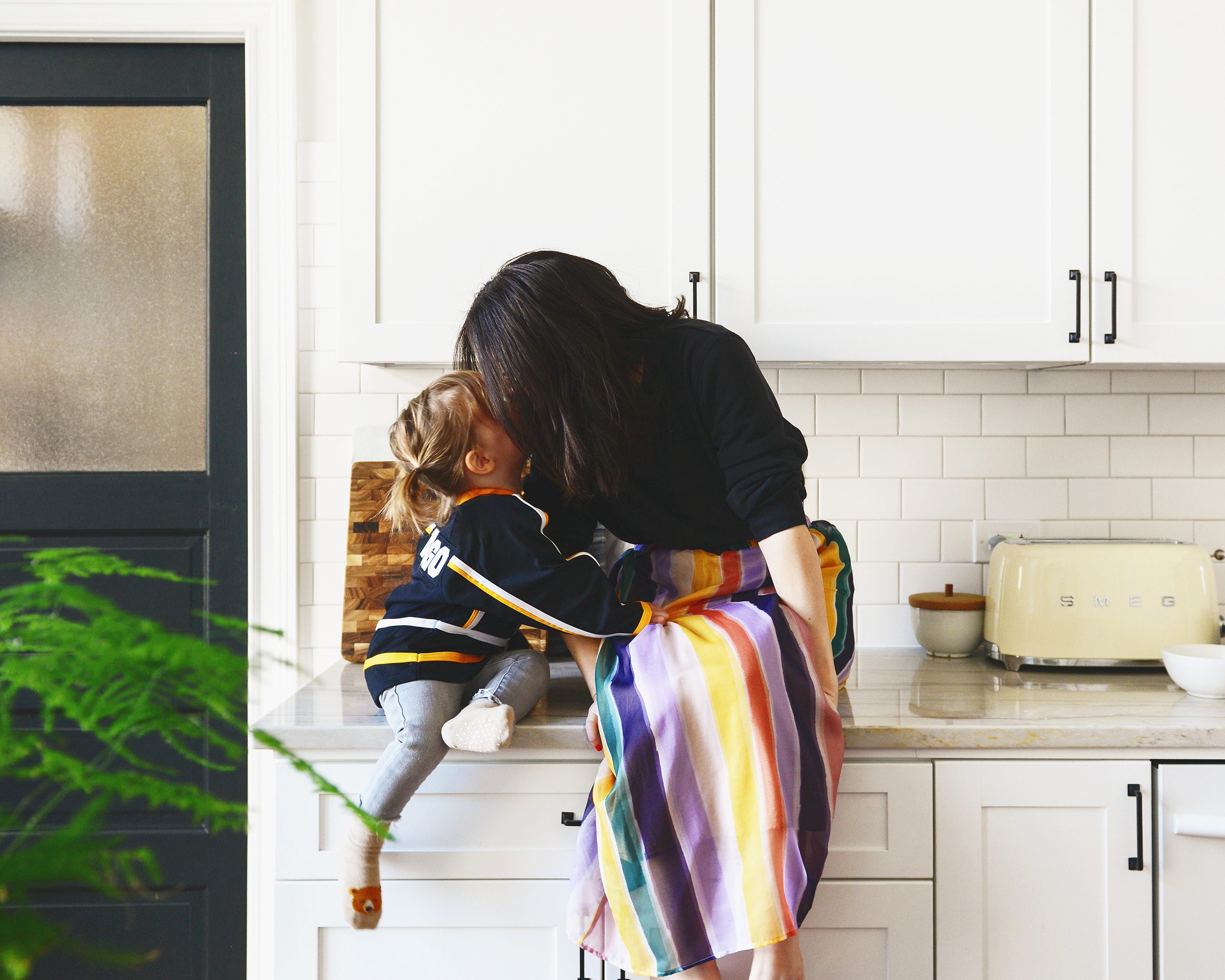 Kim and Lucy give kisses from the kitchen counter, Lucy wears her favorite Penguins jersey and Kim wears a rainbow skirt | via Yellow Brick Home