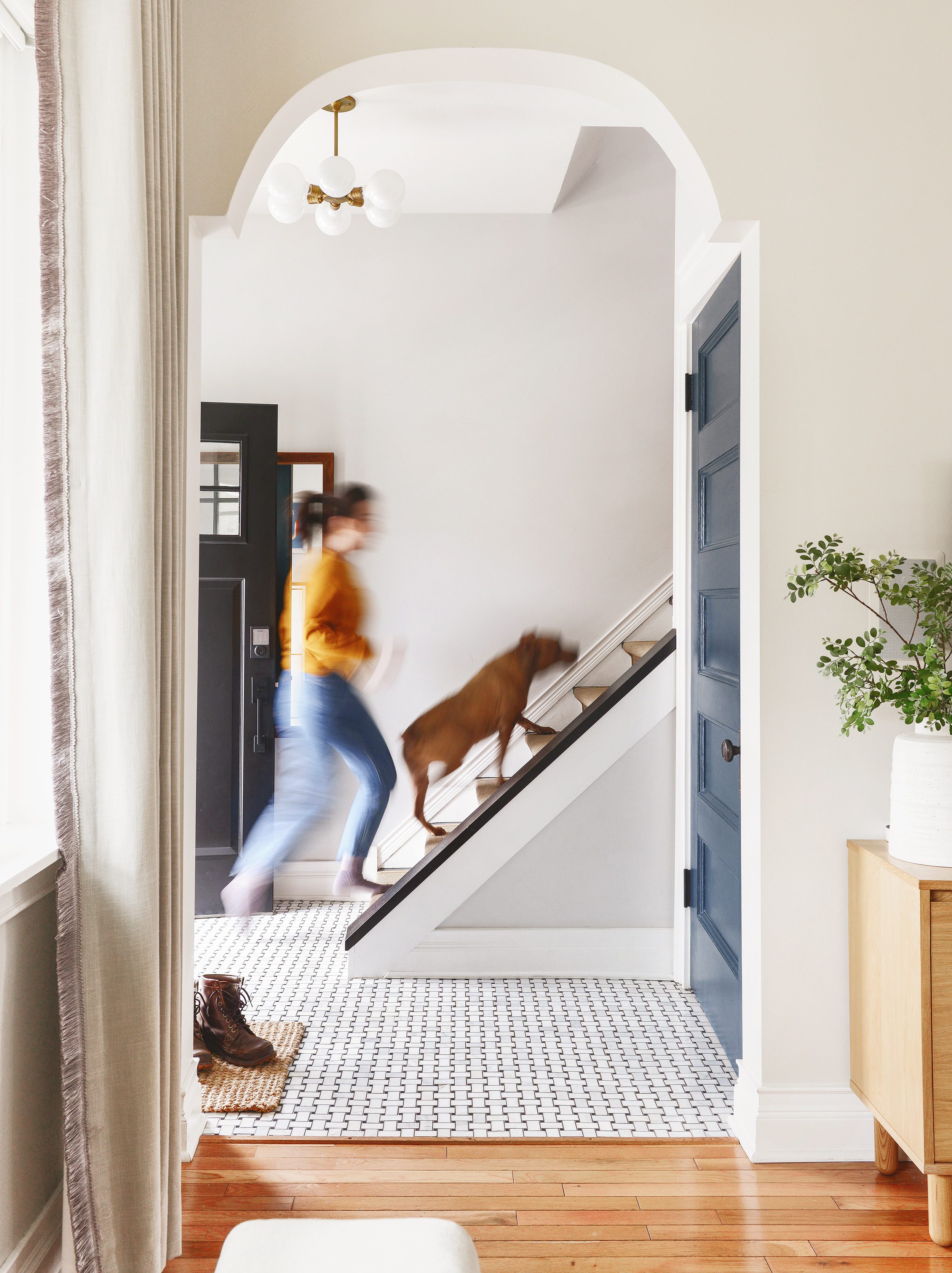 A woman and a brown pitbull dog walk quickly up the first stairs in a Chicago home's foyer // via yellow brick home