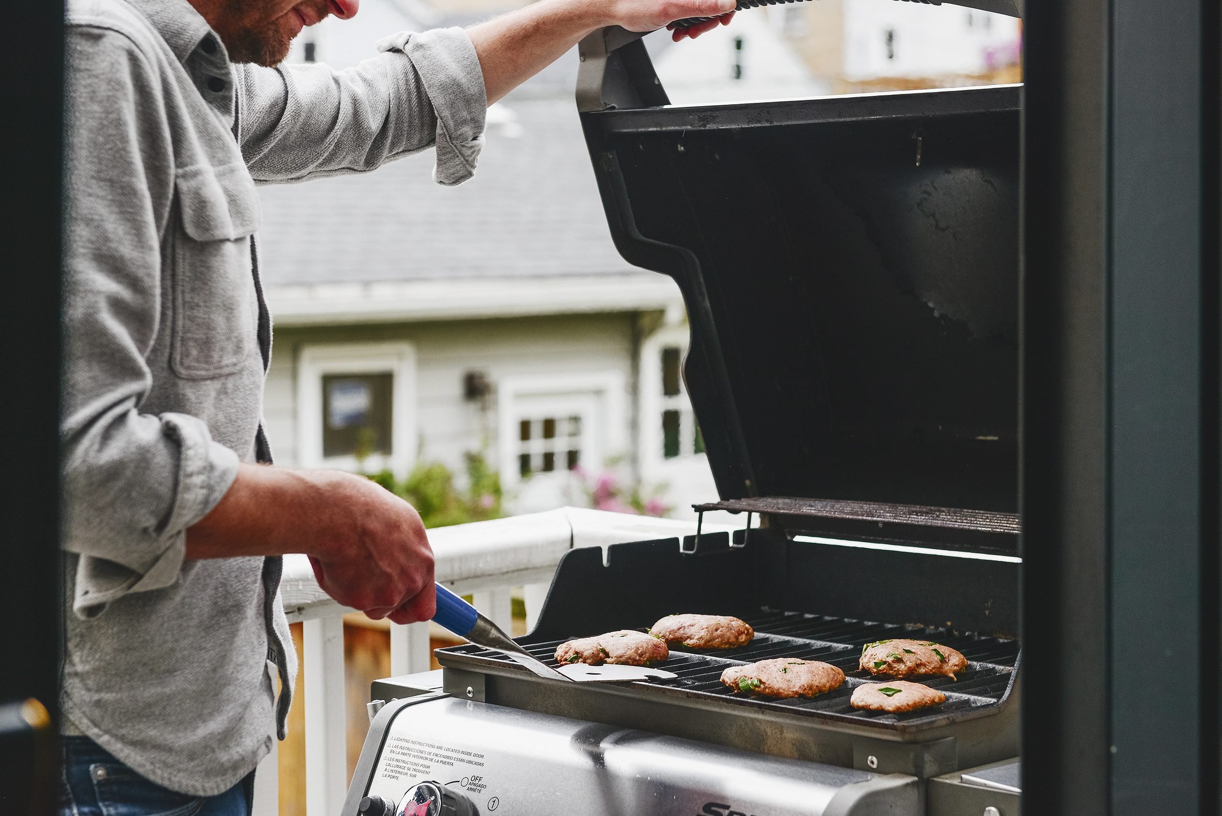 A man grills turkey burgers on a freshly cleaned weber gas grill // via yellow brick home