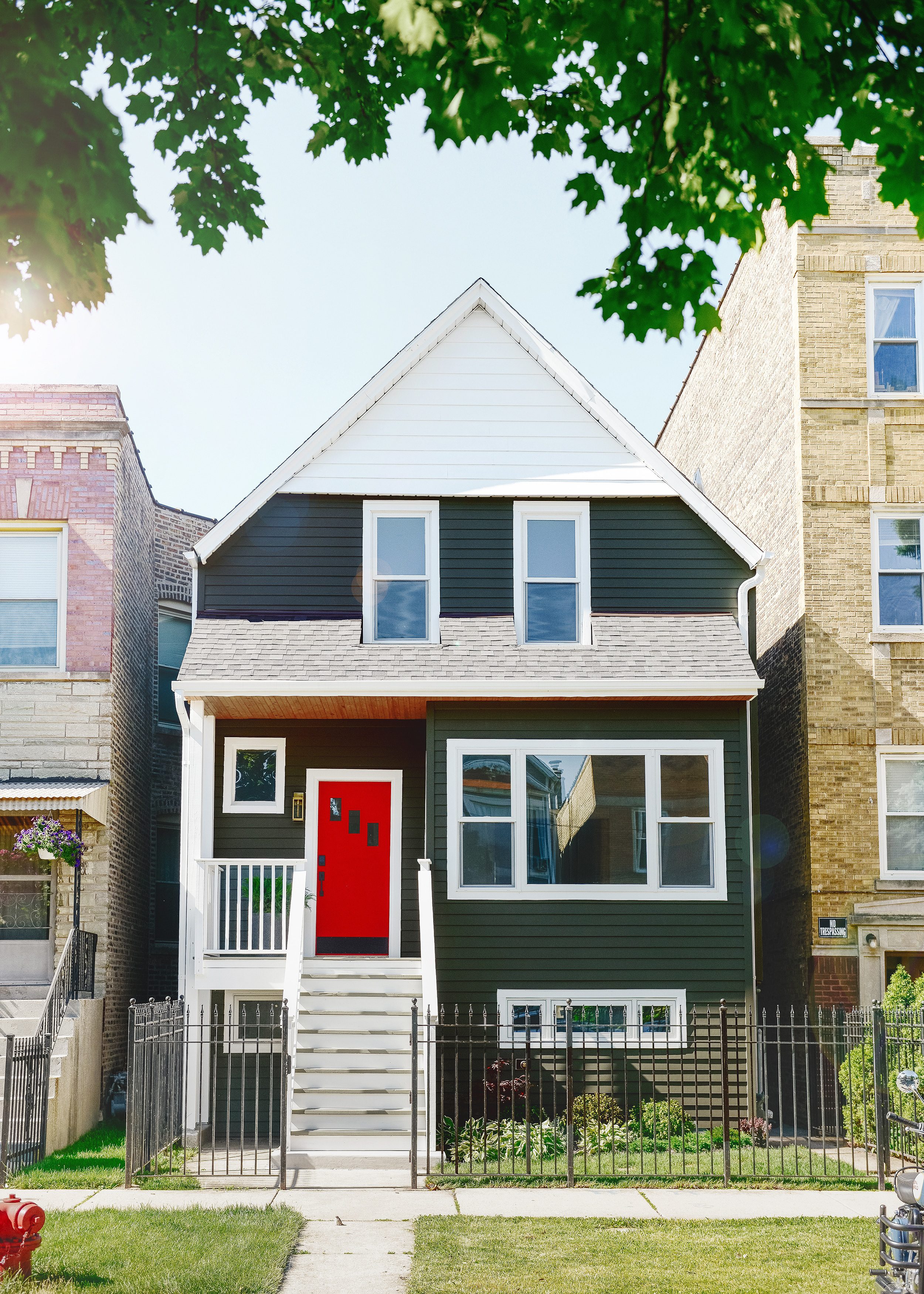 A dark green home with white trim and a red front door sits between two brick buildings on a residential Chicago block // via Yellow Brick Home