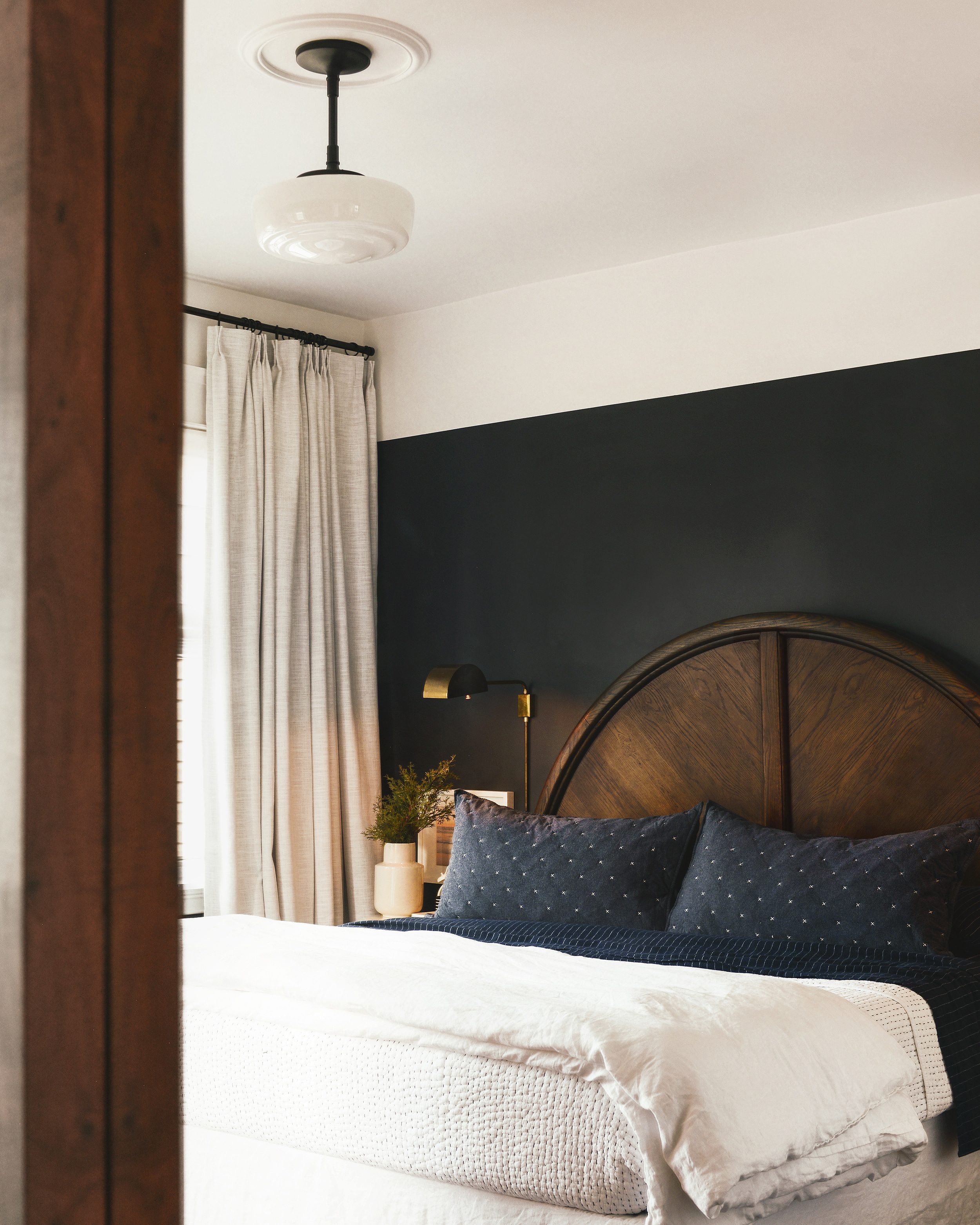 A bedroom with black walls, navy bedding and a round wooden headboard | via Yellow Brick Home
