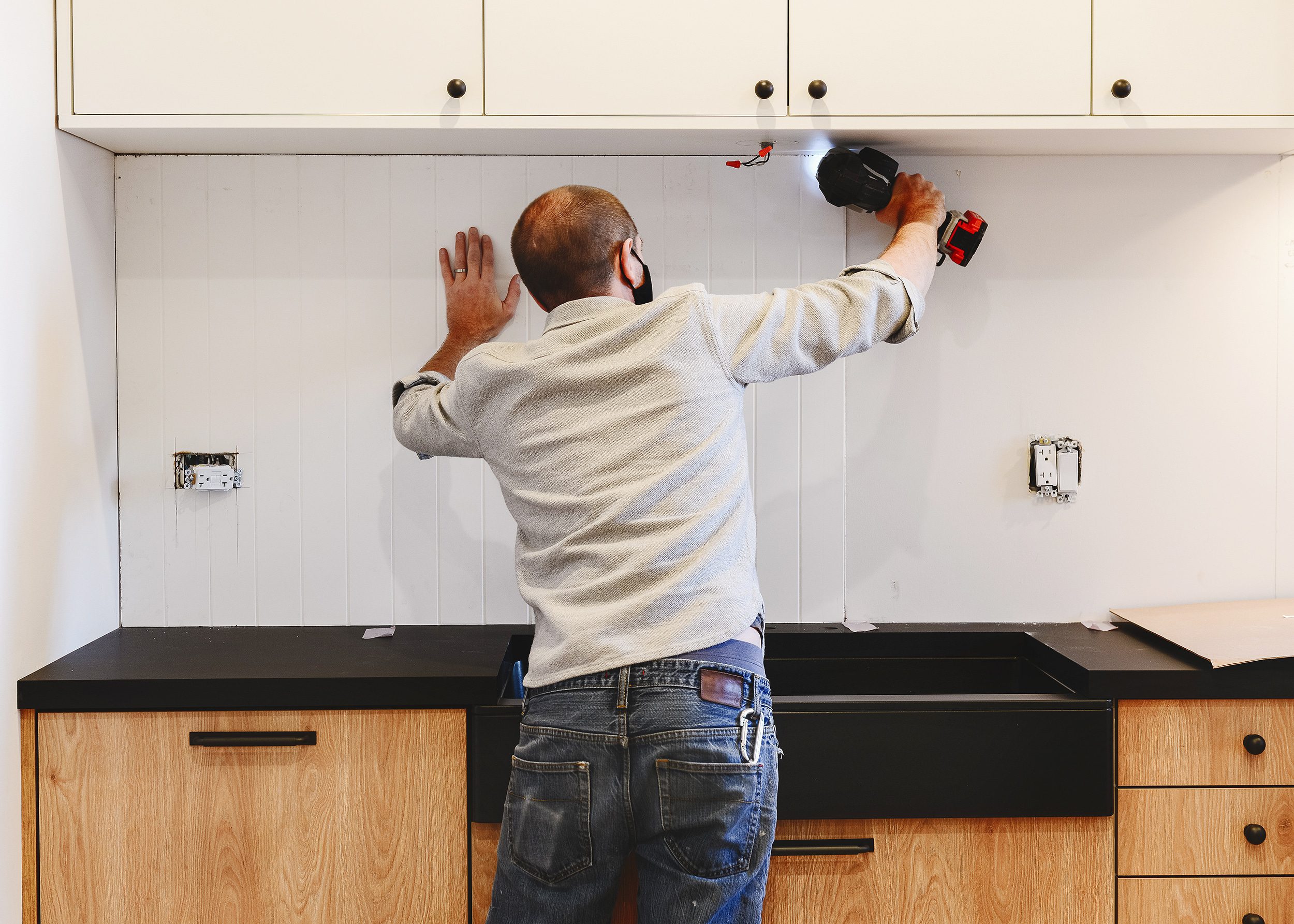 An MDF beadboard panel is installed between cabinets and countertops using a cordless nailer.