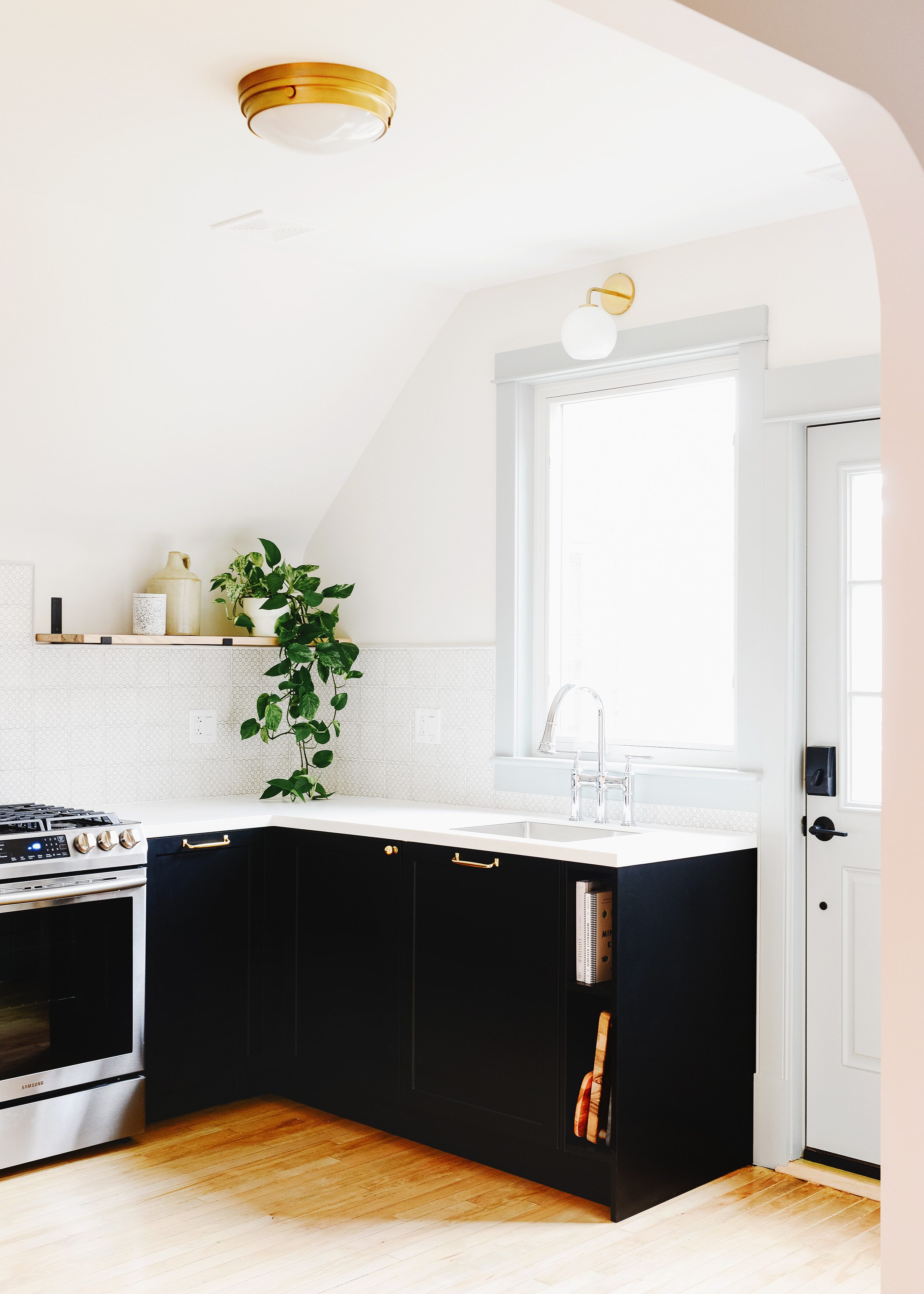 A small kitchen with black base cabinets, square tile, brass hardware and open shelving. | via Yellow Brick Home