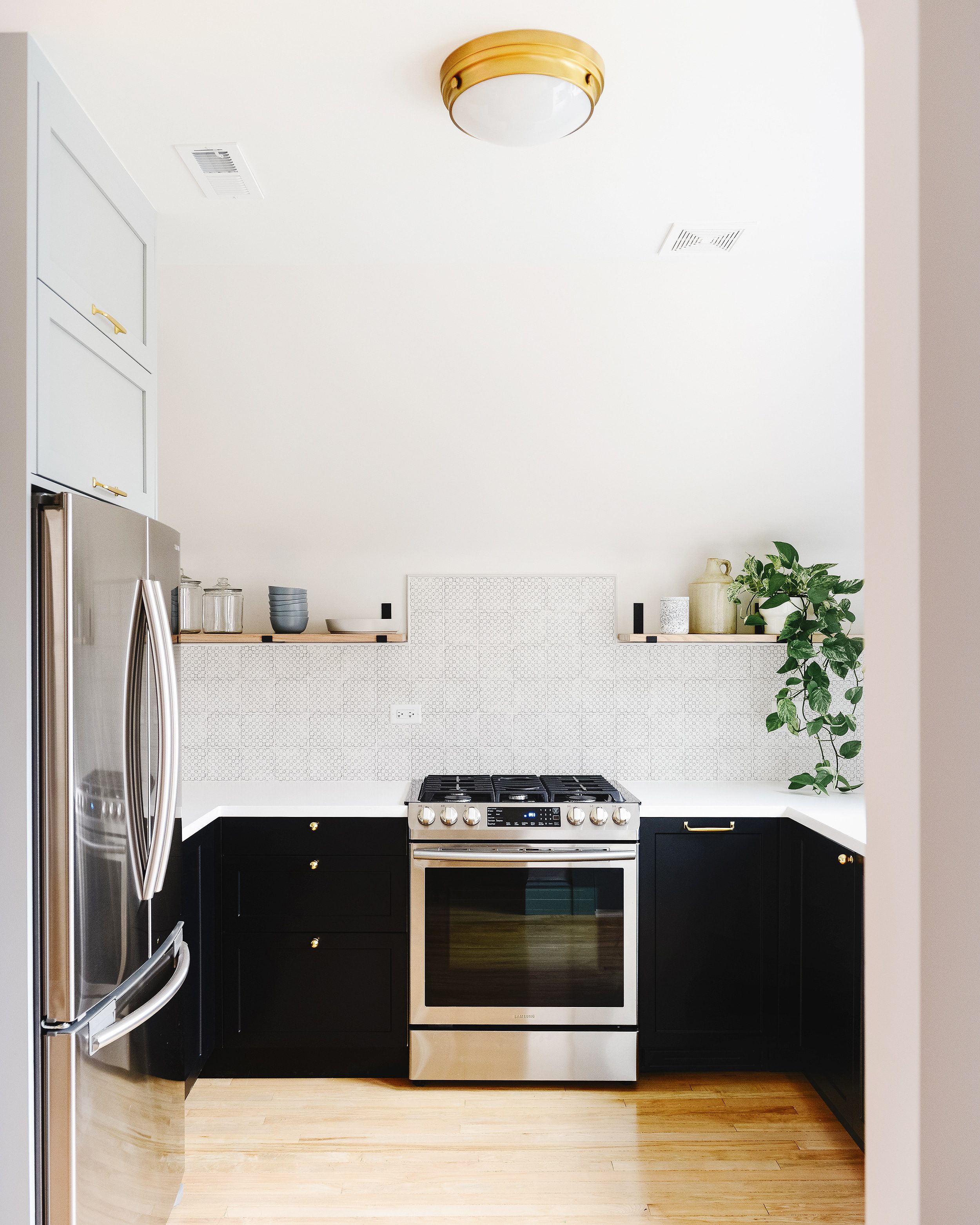 A small kitchen with black base cabinets, square tile, brass hardware and open shelving. | via Yellow Brick Home