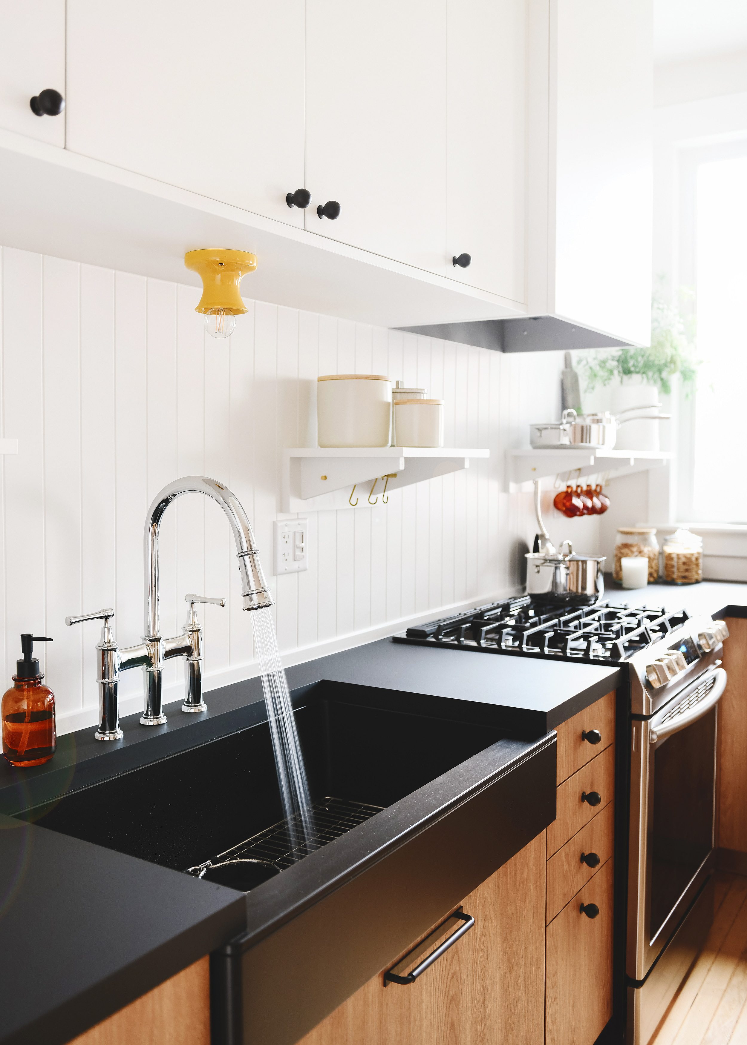 Elkay Explore bridge faucet with a Quartz Luxe apron front sink in a caviar finish, wood-toned cabinetry and black countertop | via Yellow Brick Home