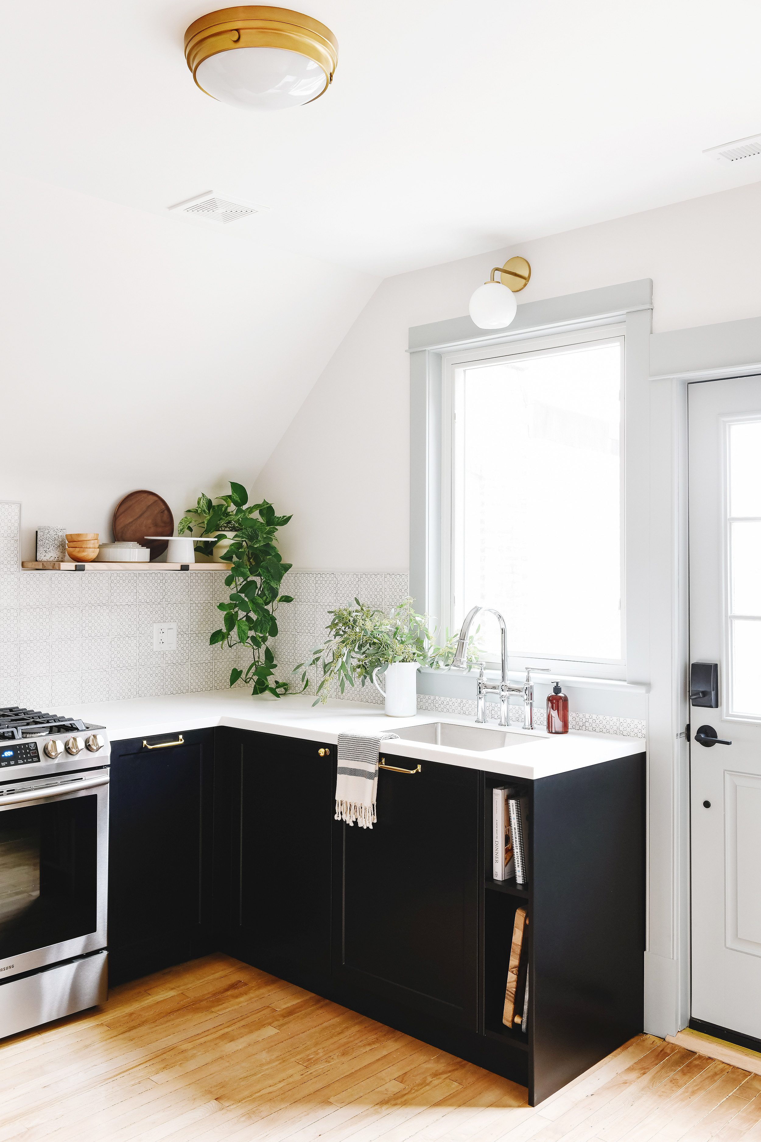 The Two Flat's Unit 2 kitchen featuring contrasting trim, black cabinetry with white countertops, a stainless range and a chrome bridge faucet // via Yellow Brick Home