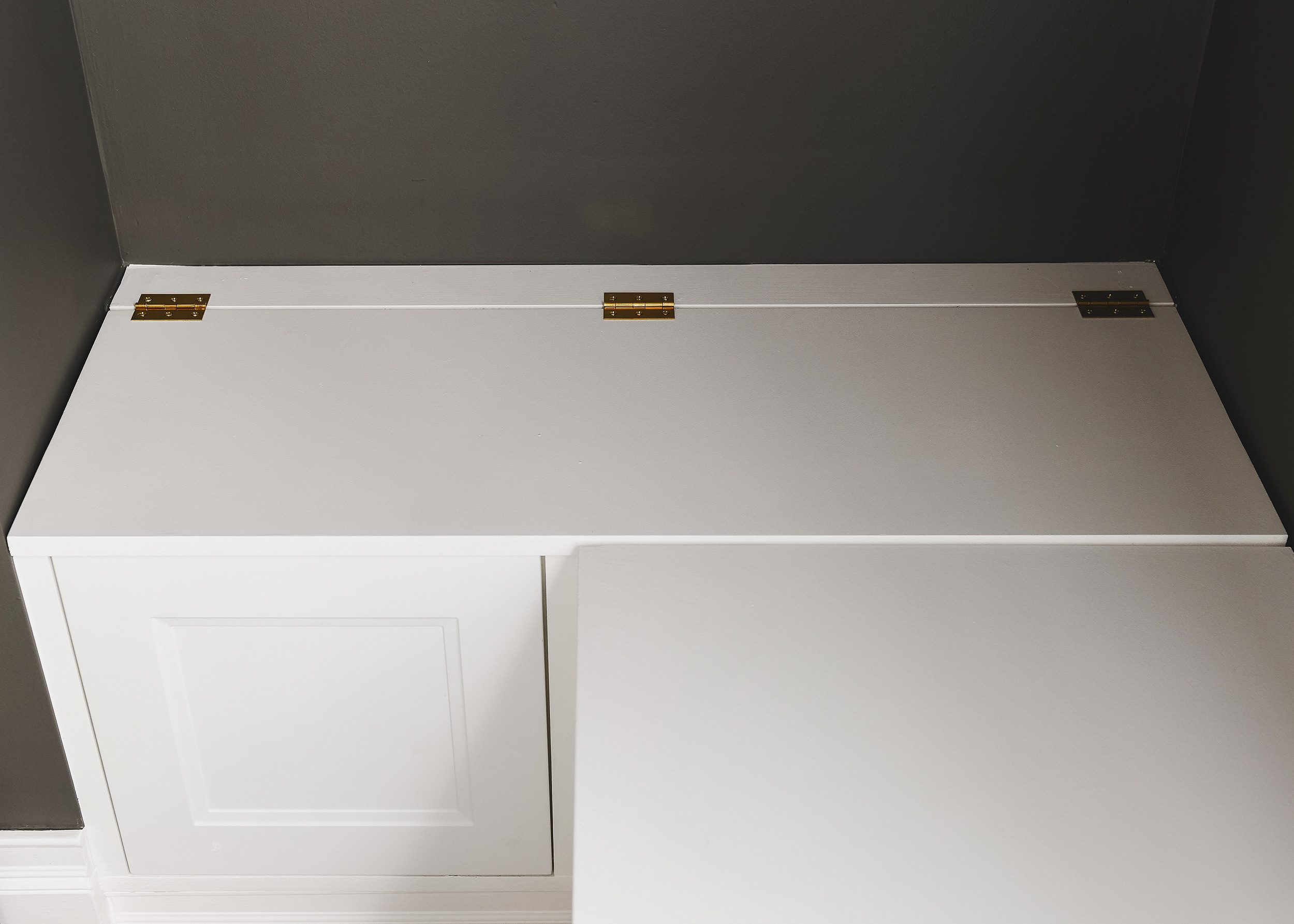 A closeup of the toy box lid, hinges and false front panel on the short end of our L-shaped built in // via Yellow Brick Home