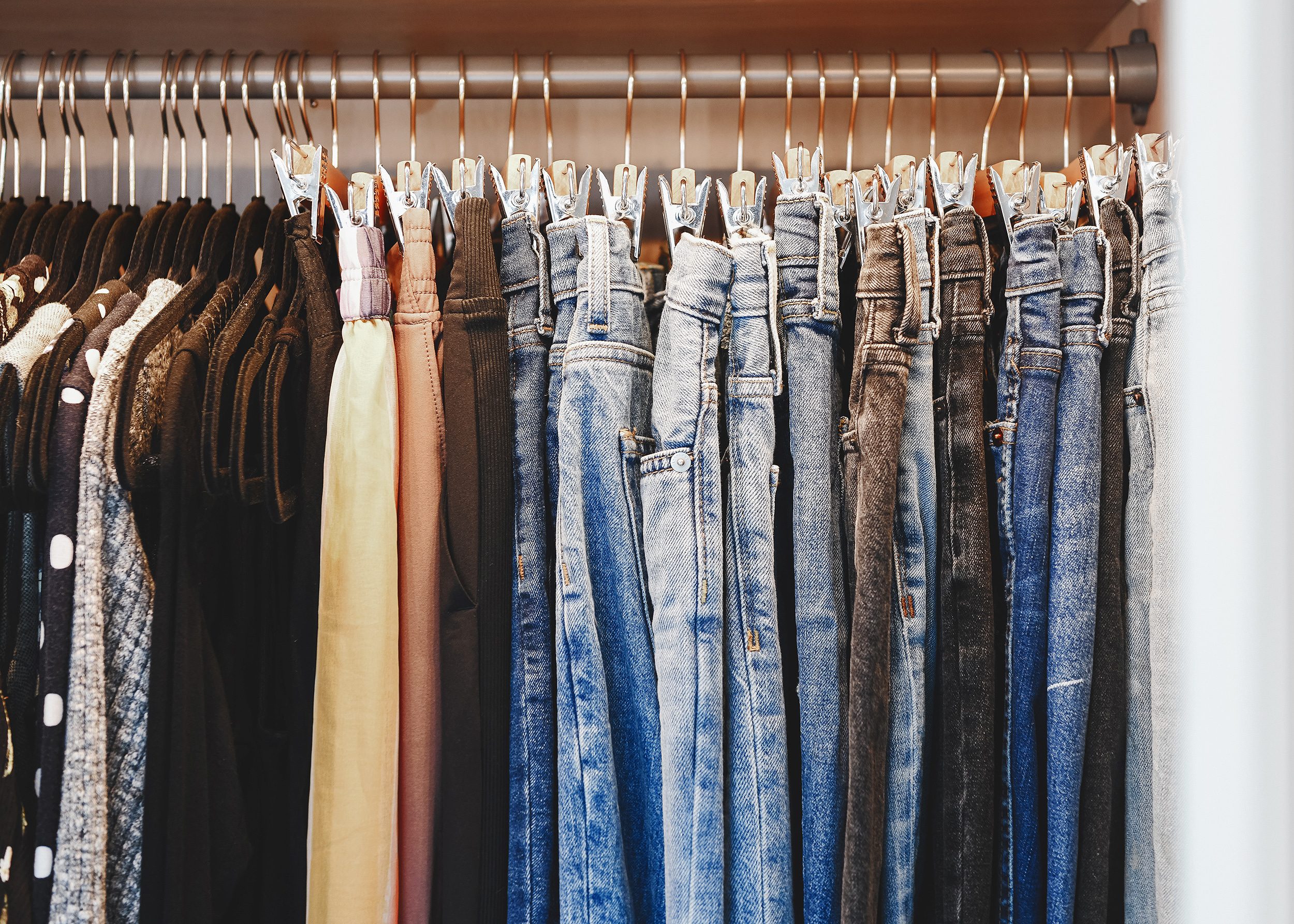 A row of clothing neatly organized in a closet, jeans hanging from pants hangers | via Yellow Brick Home