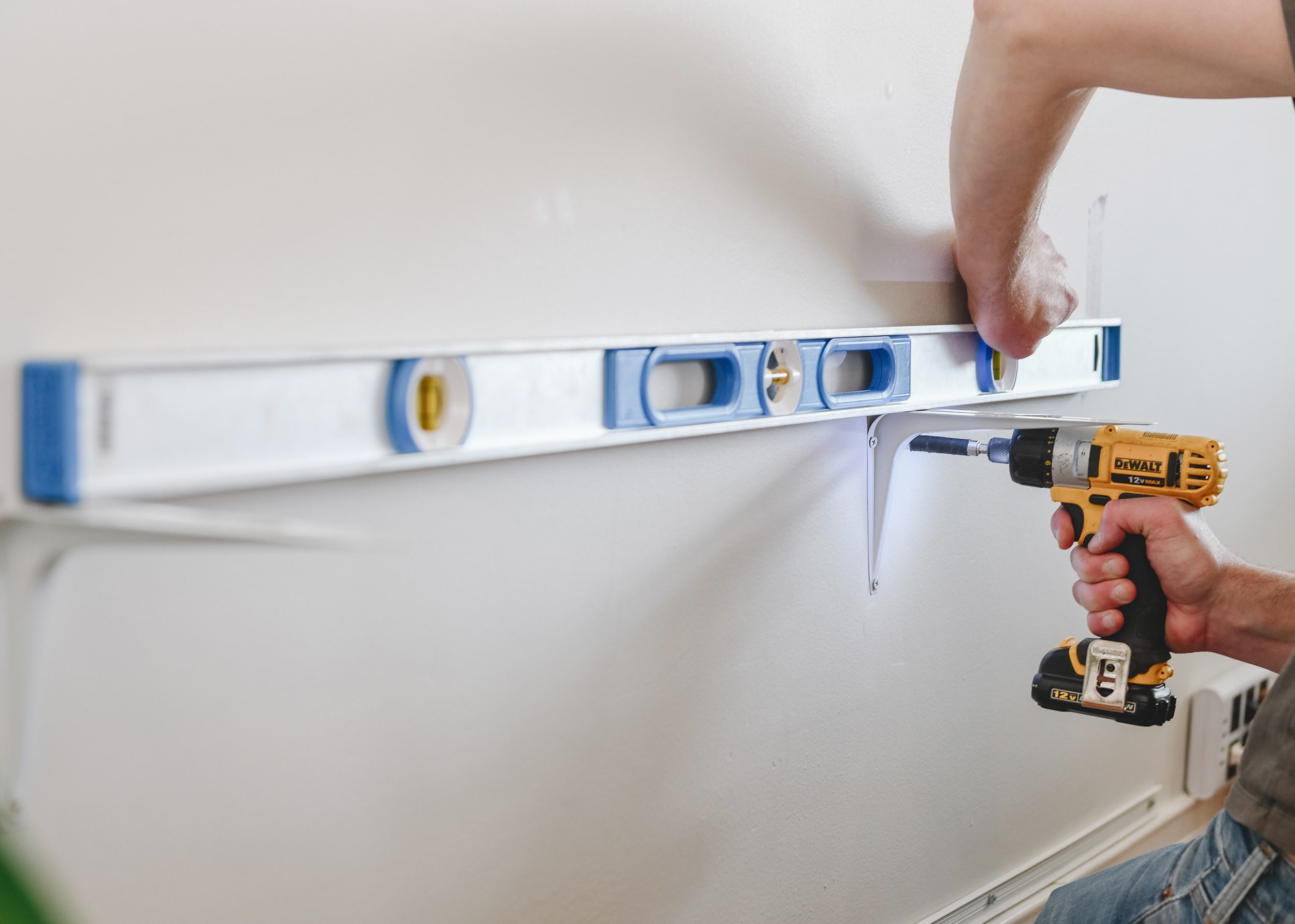 Scott uses a 48" level to ensure that each shelf bracket is aligned with the one next to it prior to screwing into the studs // via Yellow Brick Home