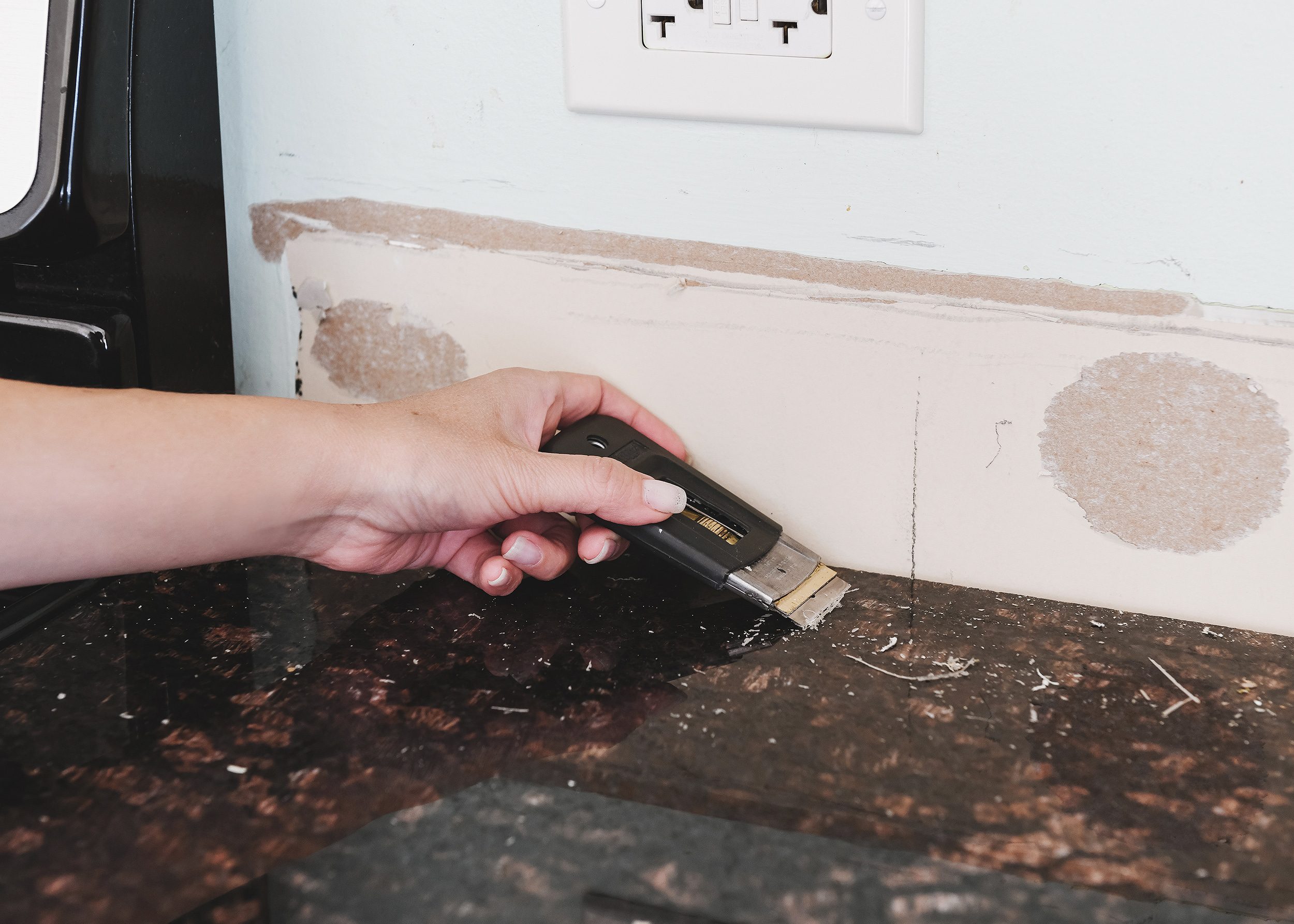Kim uses a razor blade in a retractable handle to remove excess caulk from the countertop surface. 