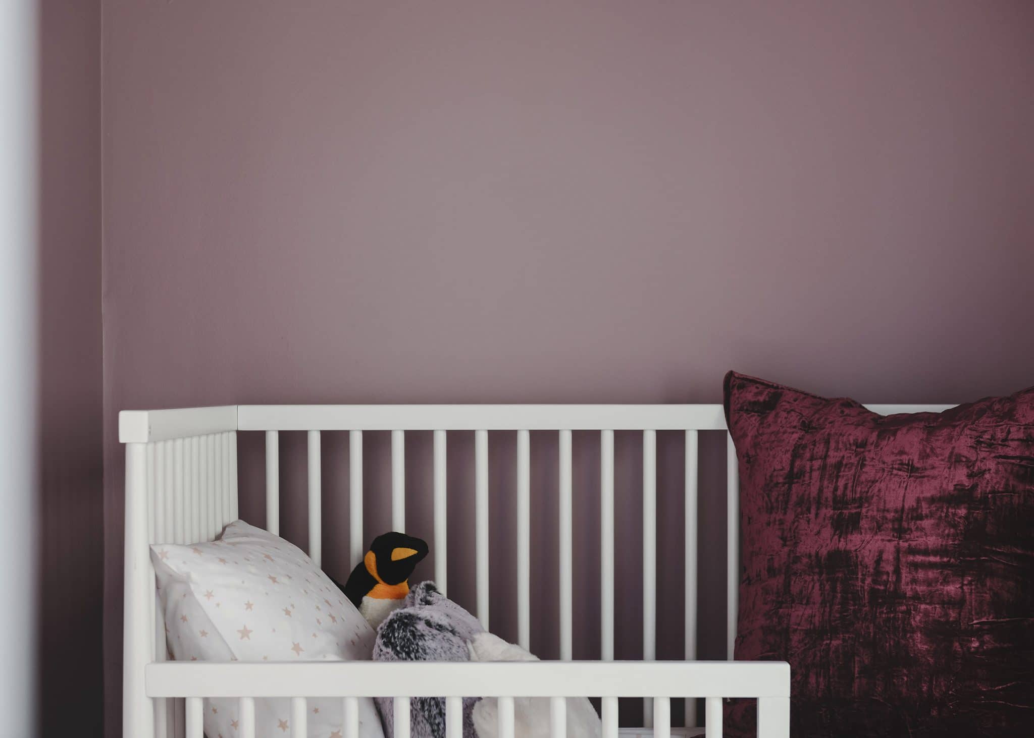 Lucy's crib against a purple wall with a crushed vrlvet pillow | color is Valspar Mellow Mauve 1004-7C | via Yellow Brick Home