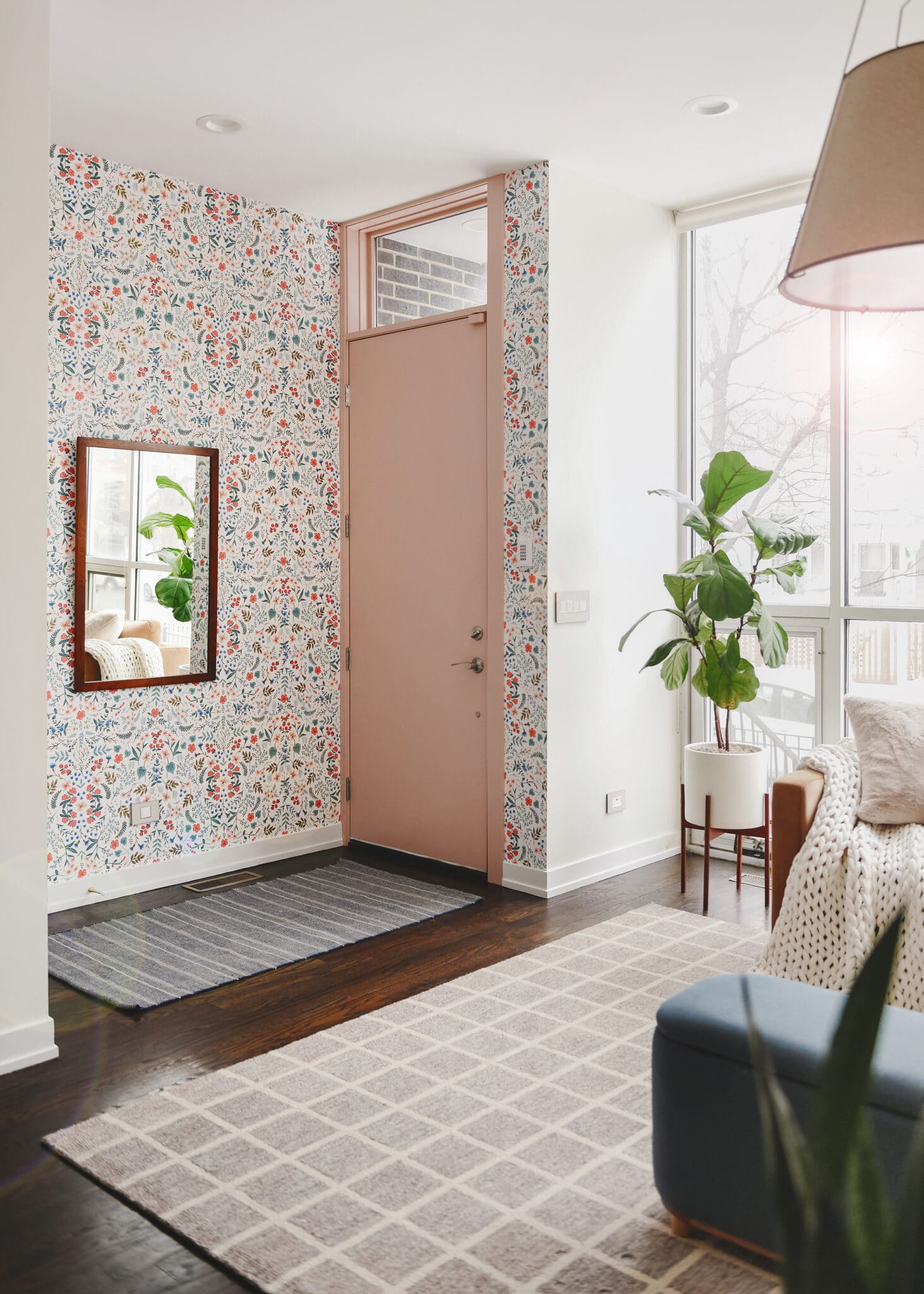 The Kalvakota's front entryway is open and airy with a pink door, colorful wallpaper and a large sectional. 