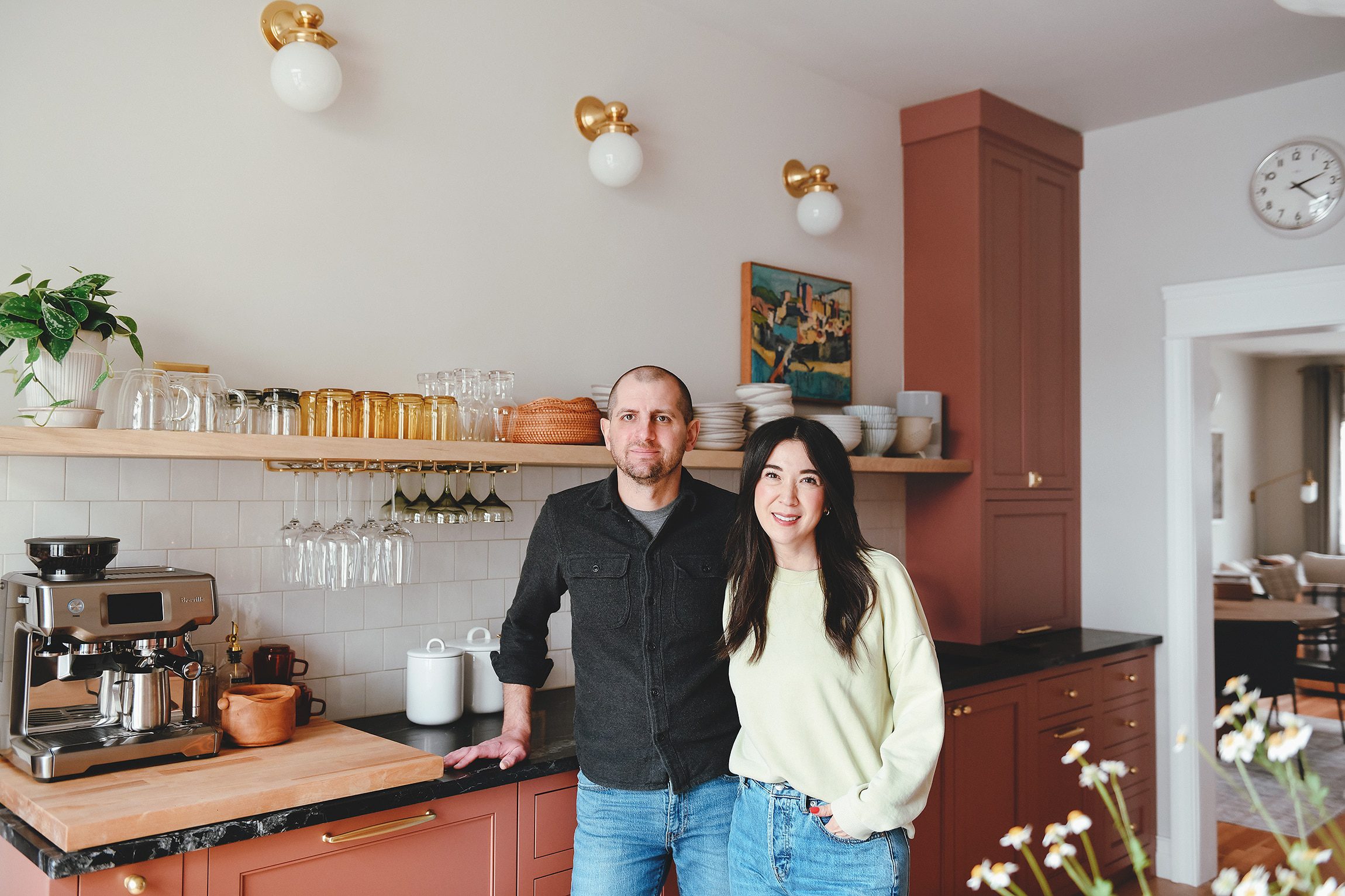 Kim and Scott in their Chicago kitchen, red cabinetry and long oak floating shelf behind them | via Yellow Brick Home