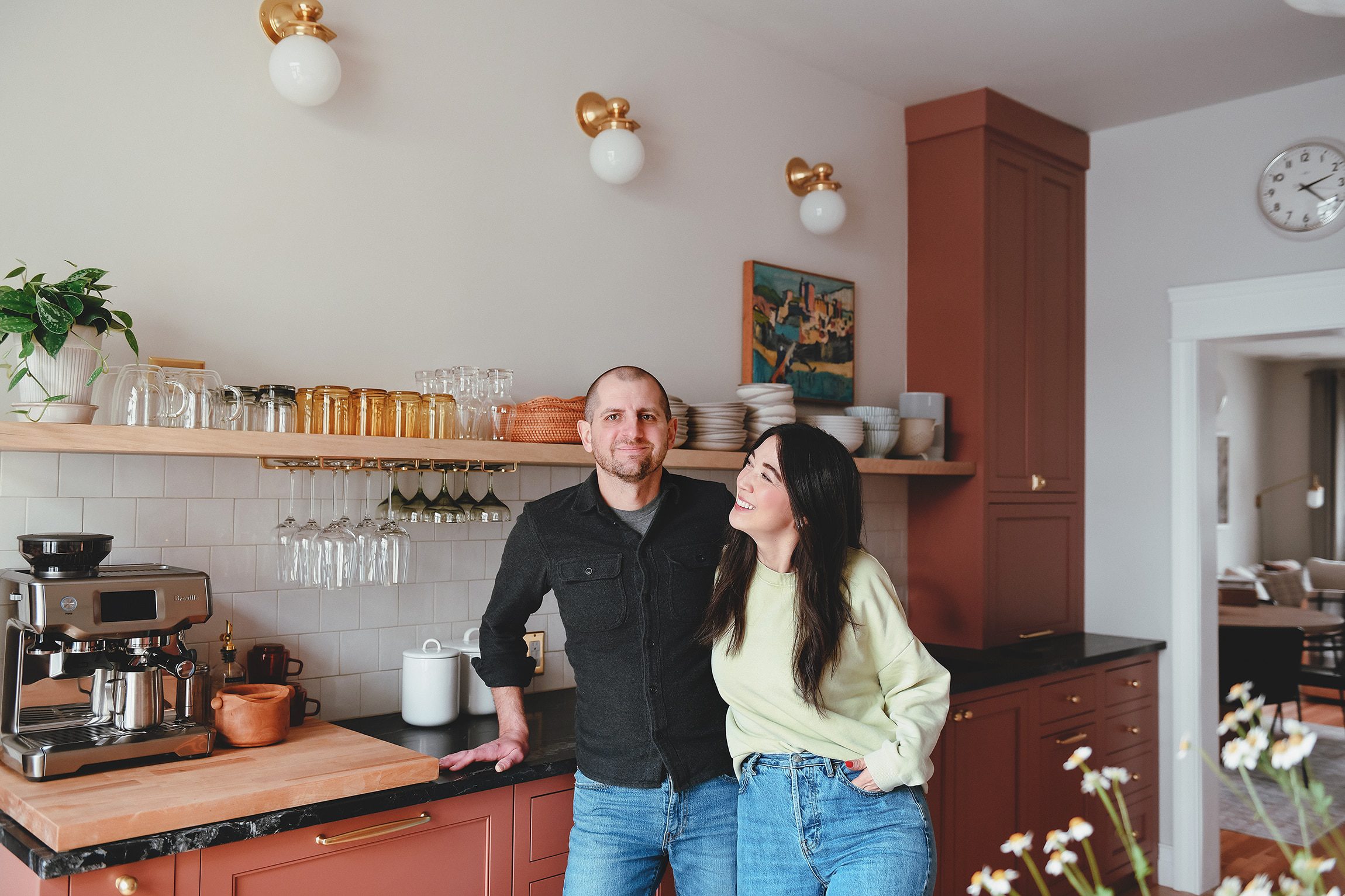 Kim and Scott in their renovated kitchen with red cabinets, black marble countertops and oak floating shelf | Our goals for 2023 | via Yellow Brick Home