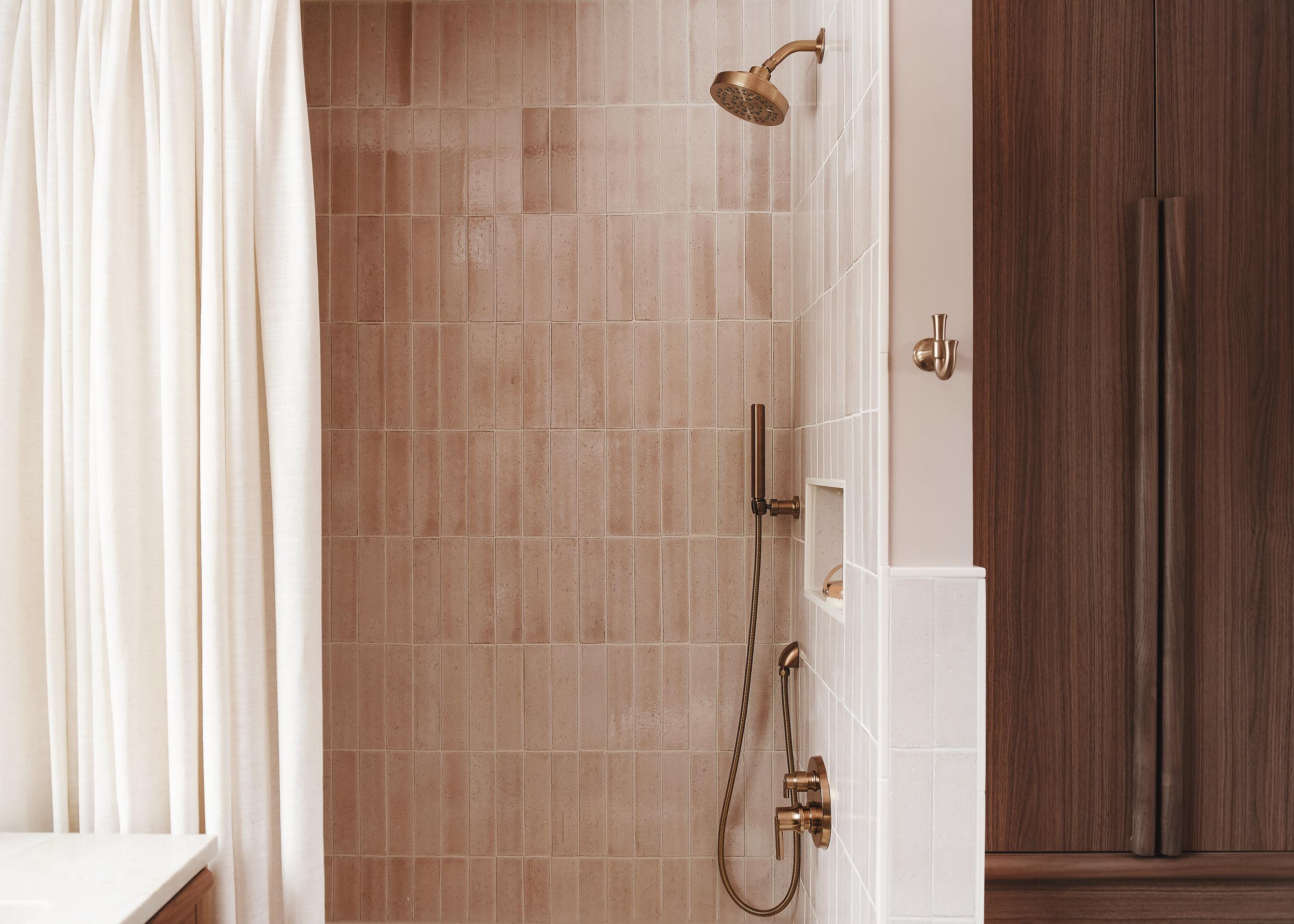 A peek into the shower with pink tile, cream shower curtain and walnut cabinetry | via Yellow Brick Home